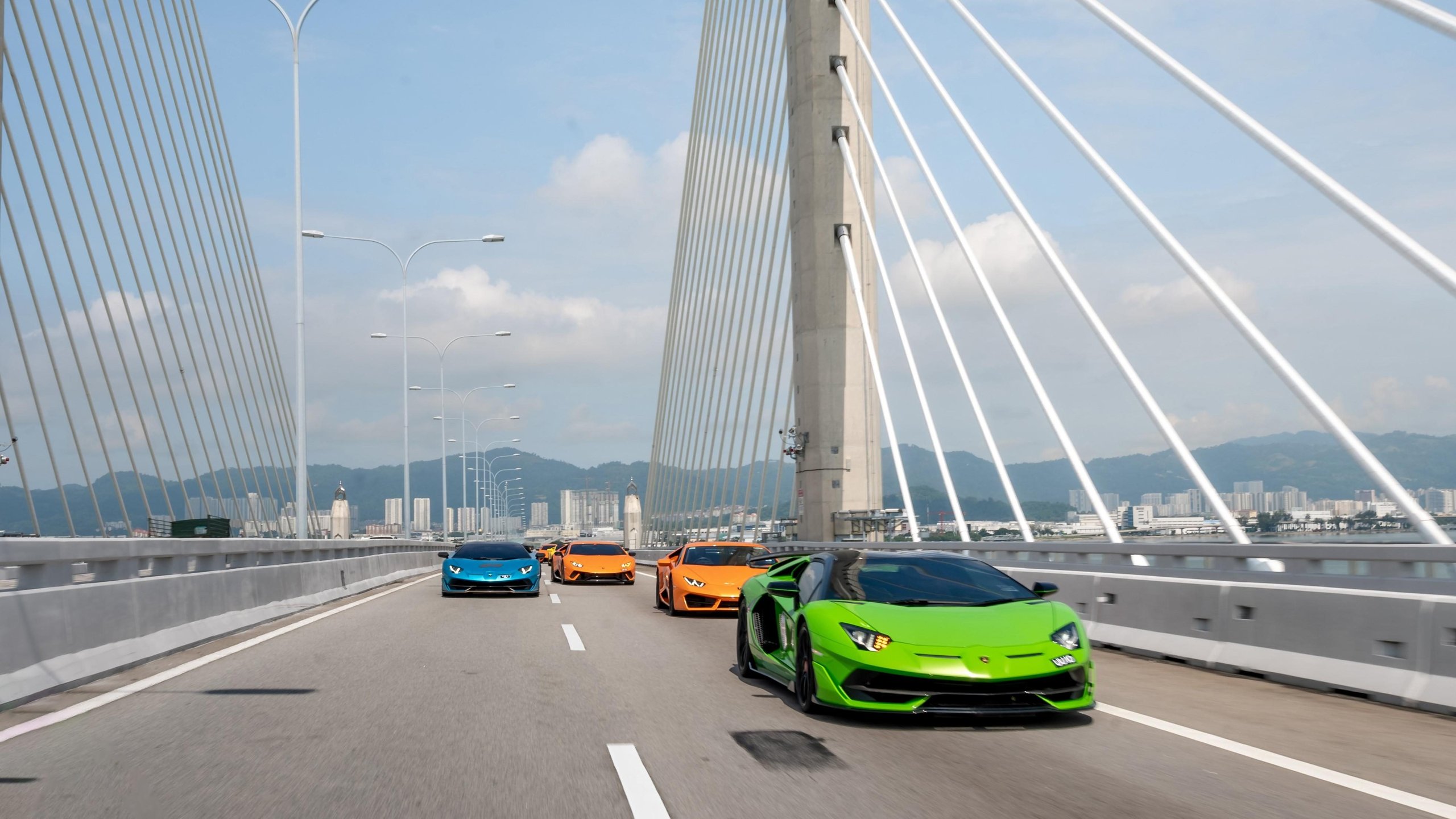 Lamborghini'S First Southeast Asia Esperienza Giro Turned Malaysia Into A Rolling 60Th Birthday Party 3 Convoy of colorful lamborghini supercars crossing a modern cable-stayed bridge with a city skyline in the background