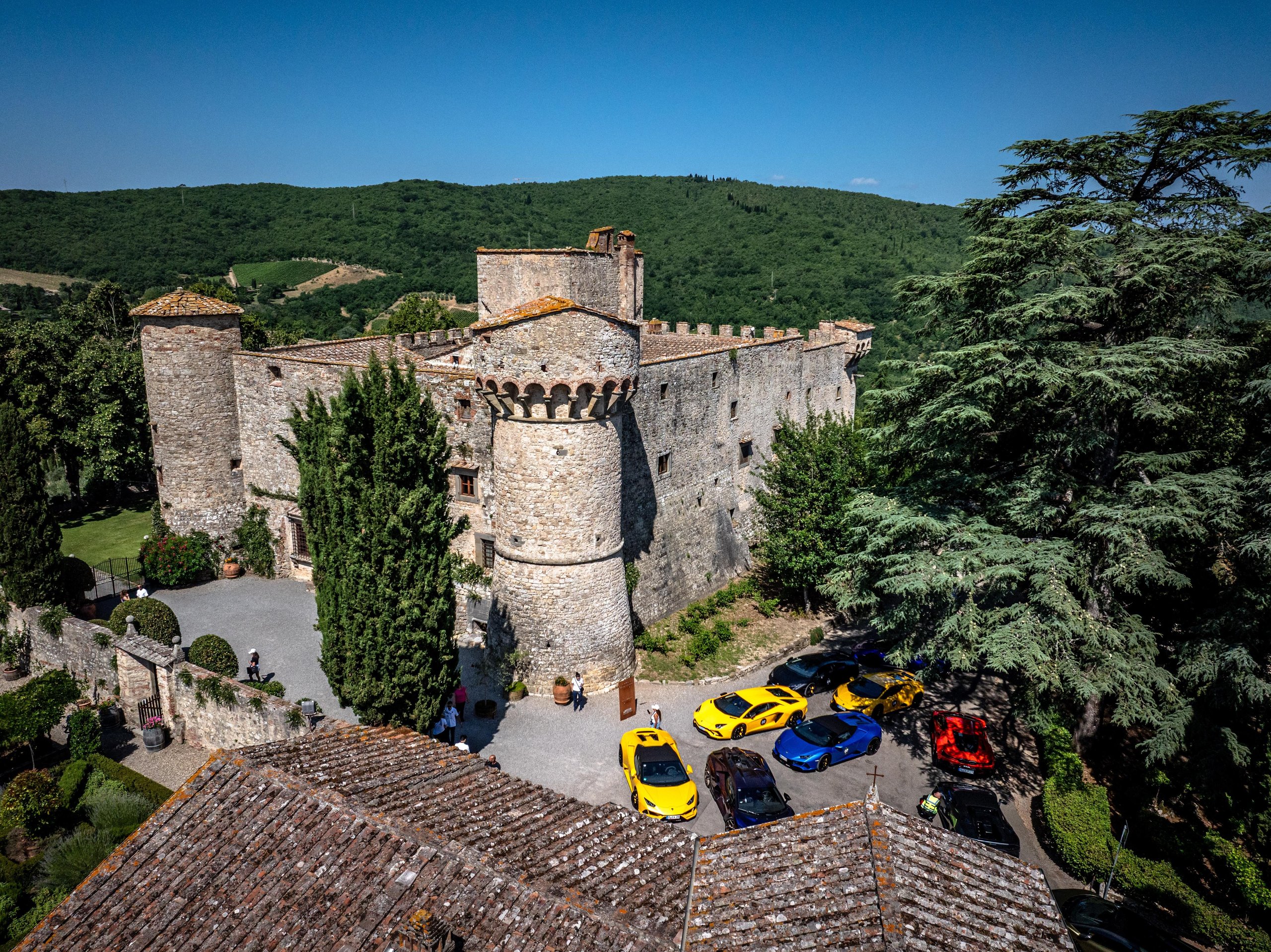 Colorful lamborghini supercars parked in front of a grand historic stone castle during esperienza giro toscana 2025