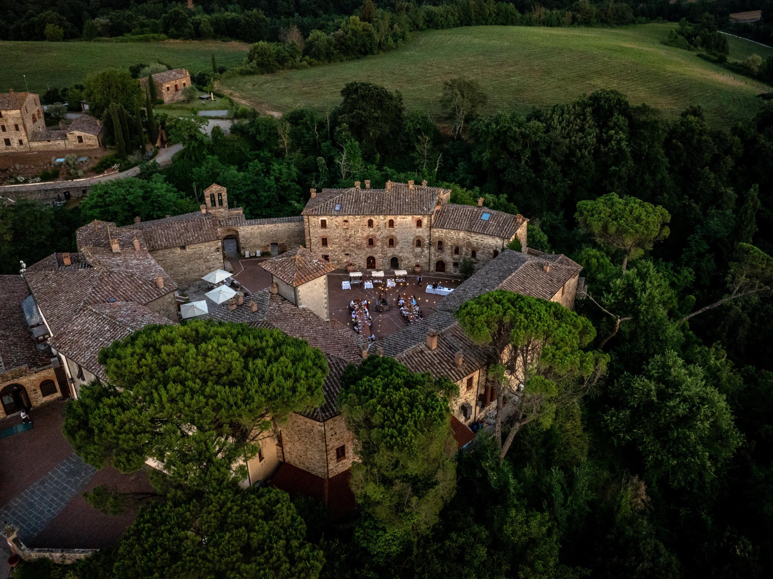 Aerial view of the historic castel monastero estate nestled in the tuscan hills with an outdoor dinner visible in the courtyard