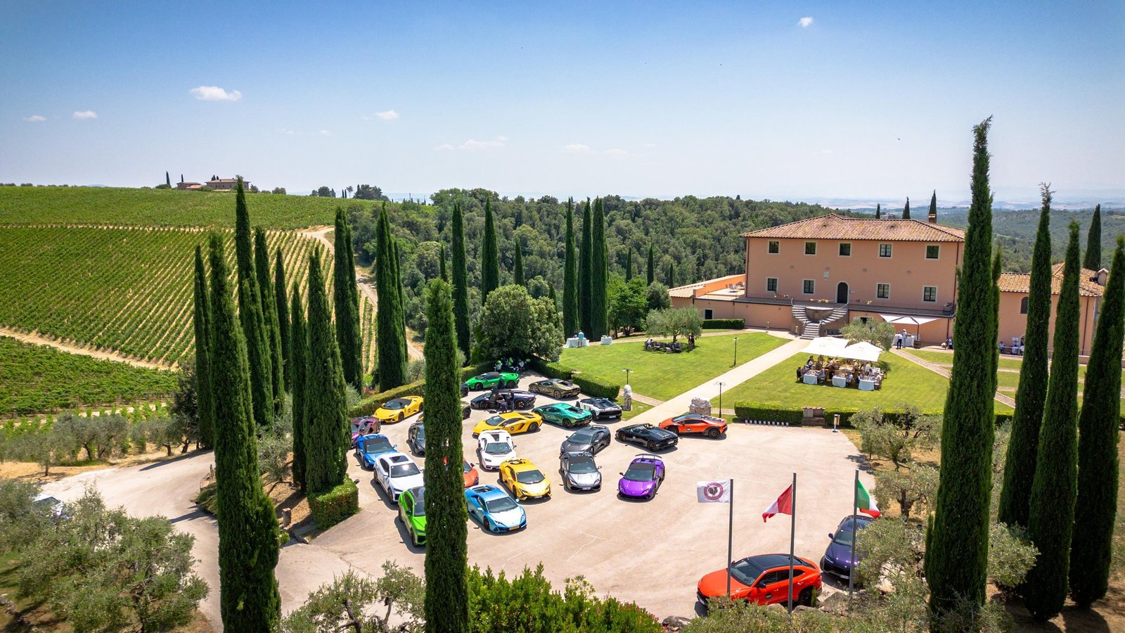 Colorful Lamborghini supercars parked at a Tuscan estate surrounded by vineyards and cypress trees during Esperienza Giro Toscana 2025