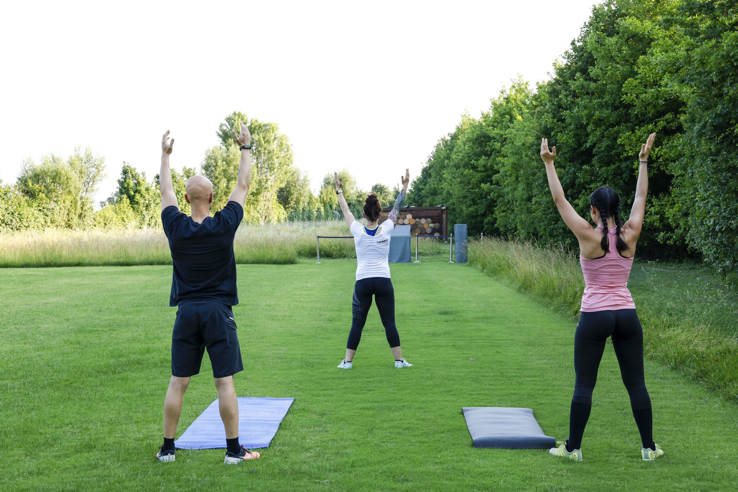 Lamborghini employees performing outdoor exercises with arms raised on yoga mats as part of FEELOSOPHY Body pillar