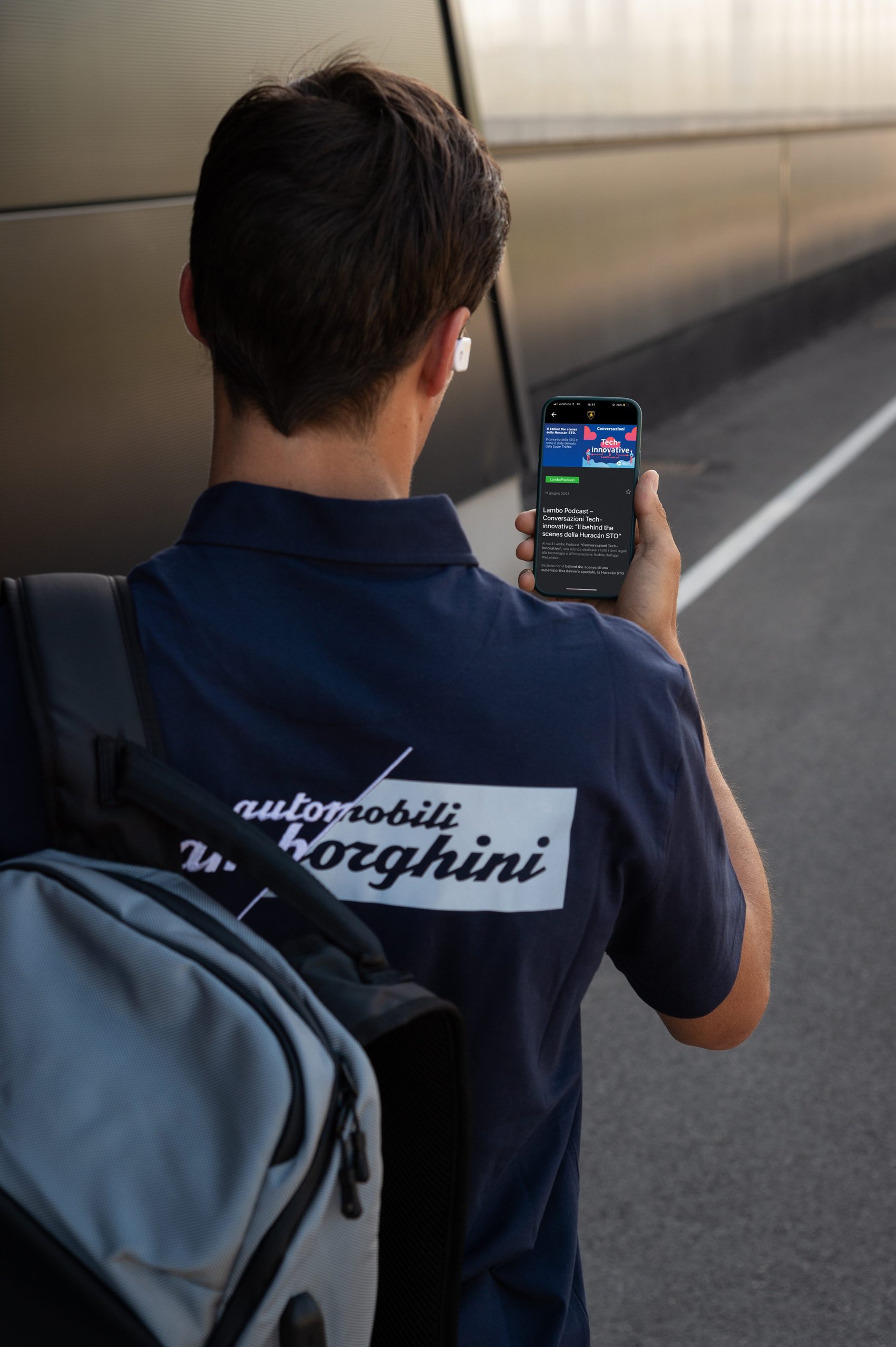 Lamborghini employee in branded polo shirt reading company news on a smartphone