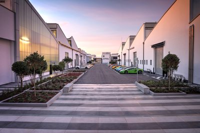 Lamborghini Puts One Executive In Charge Of Both Marketing And Sales, Hires Bugatti'S Comms Chief: Why It Matters 2 Colorful lamborghini supercars lined up along the pathway at the sant'agata bolognese factory complex at dusk