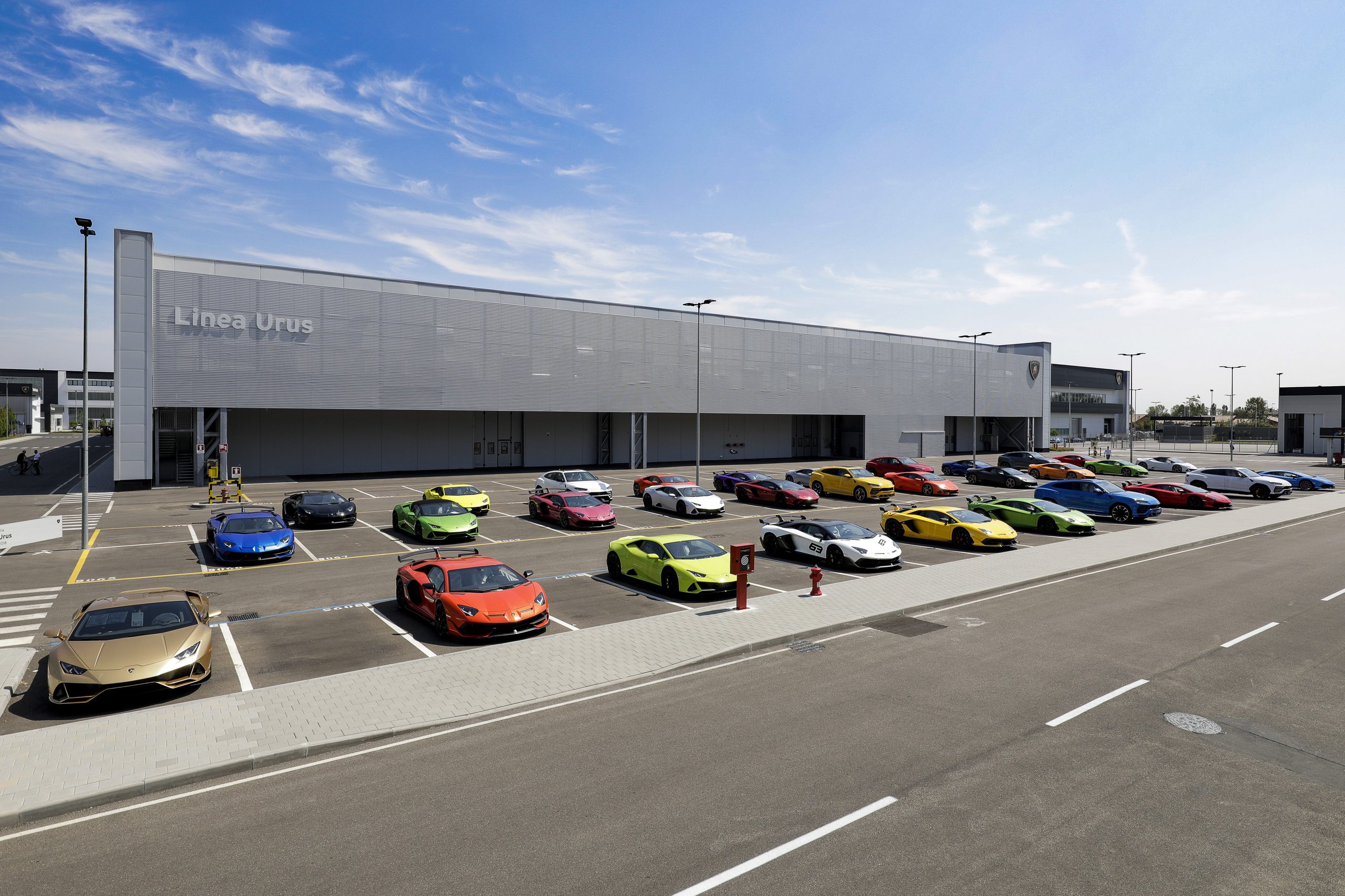 Lamborghini Puts One Executive In Charge Of Both Marketing And Sales, Hires Bugatti'S Comms Chief: Why It Matters 9 Aerial view of colorful lamborghini supercars and urus suvs parked in front of the linea urus factory building