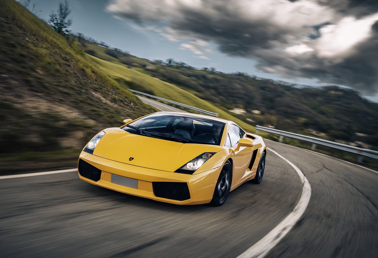 Yellow Lamborghini Gallardo driving on a winding mountain road under dramatic skies