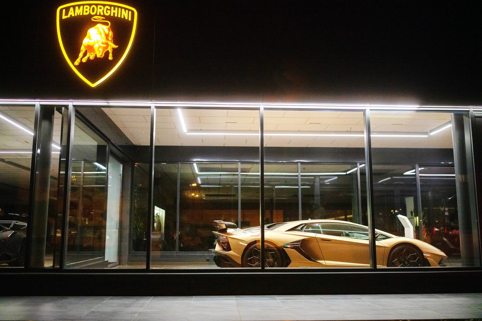 Gold Lamborghini Aventador SVJ displayed in the illuminated glass showroom of Lamborghini Geneva at night