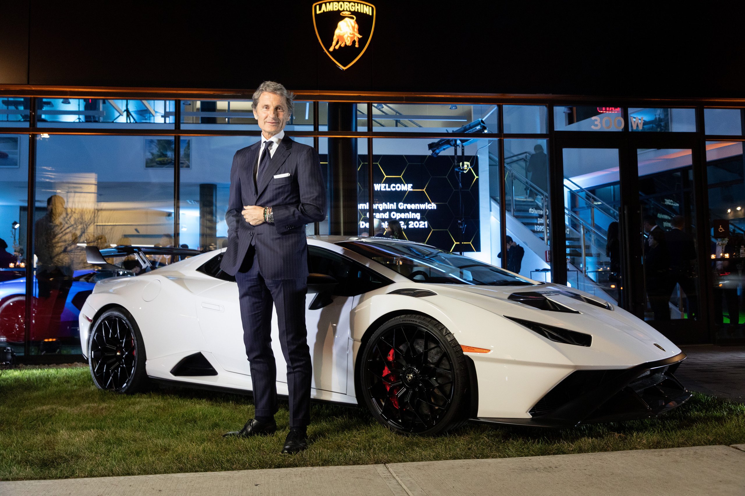 Lamborghini Greenwich Opens With A Proper Ad Personam Studio, And That Matters More Than The Ribbon Cutting 11 Stephan winkelmann standing beside a white lamborghini huracán sto outside the greenwich showroom at night with the lamborghini shield logo above