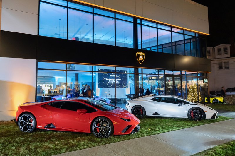 Red Lamborghini Huracán STO and white Huracán EVO parked outside the illuminated Lamborghini Greenwich showroom at night