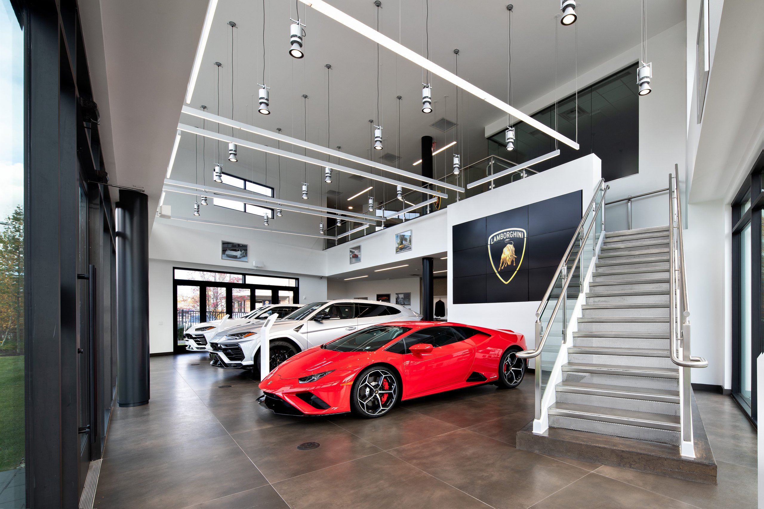 Lamborghini Greenwich Opens With A Proper Ad Personam Studio, And That Matters More Than The Ribbon Cutting 9 Interior of the lamborghini greenwich showroom featuring a red huracán evo, two urus suvs, a large lamborghini logo screen, and modern staircase
