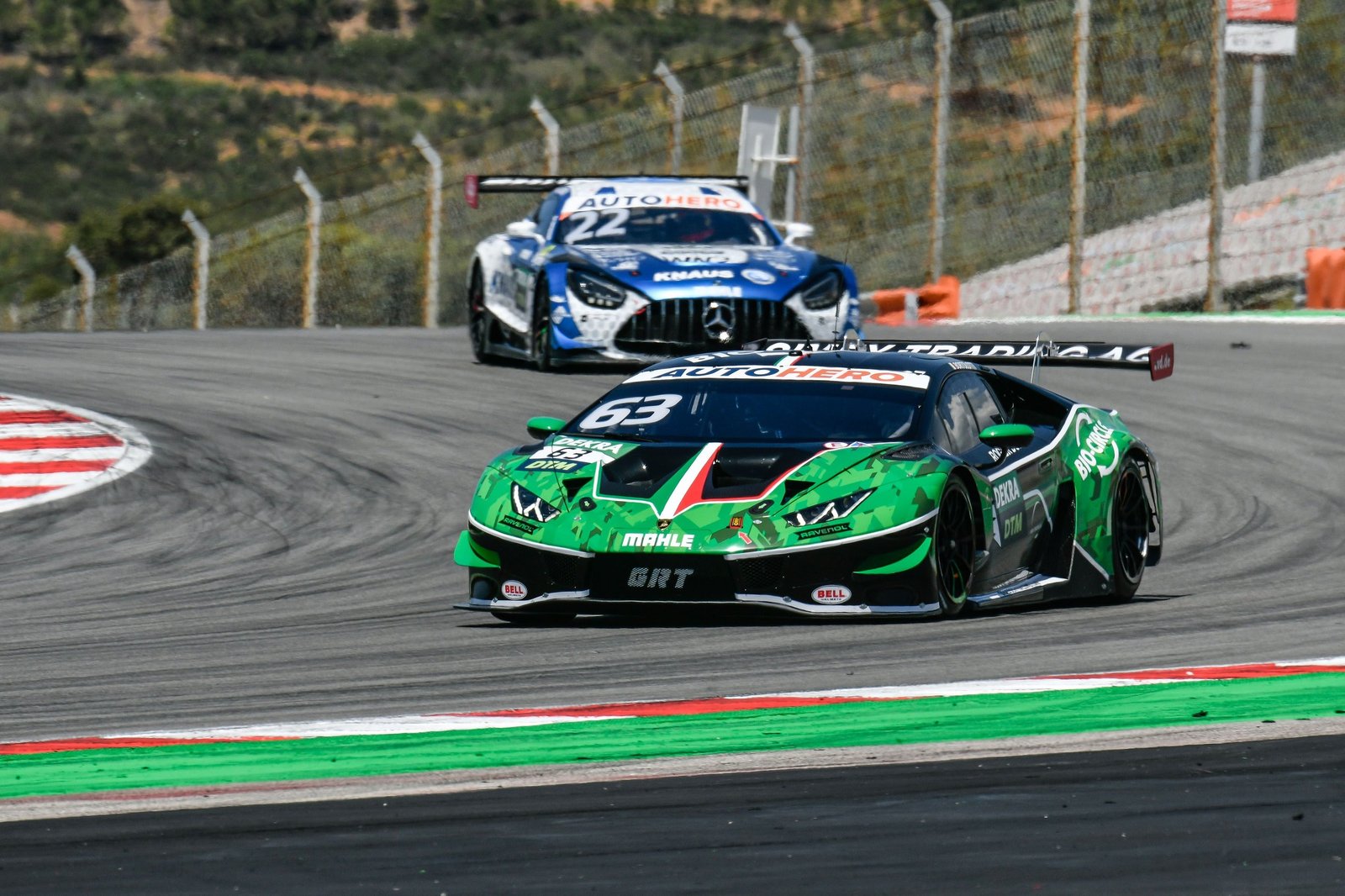 Green Lamborghini Huracán GT3 EVO number 63 cornering at Portimão with a Mercedes-AMG GT3 visible in the background during DTM competition