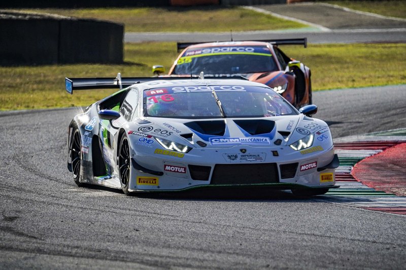 White Lamborghini Huracán GT3 EVO2 race car navigating a turn on a racetrack with sponsor decals and large rear wing visible