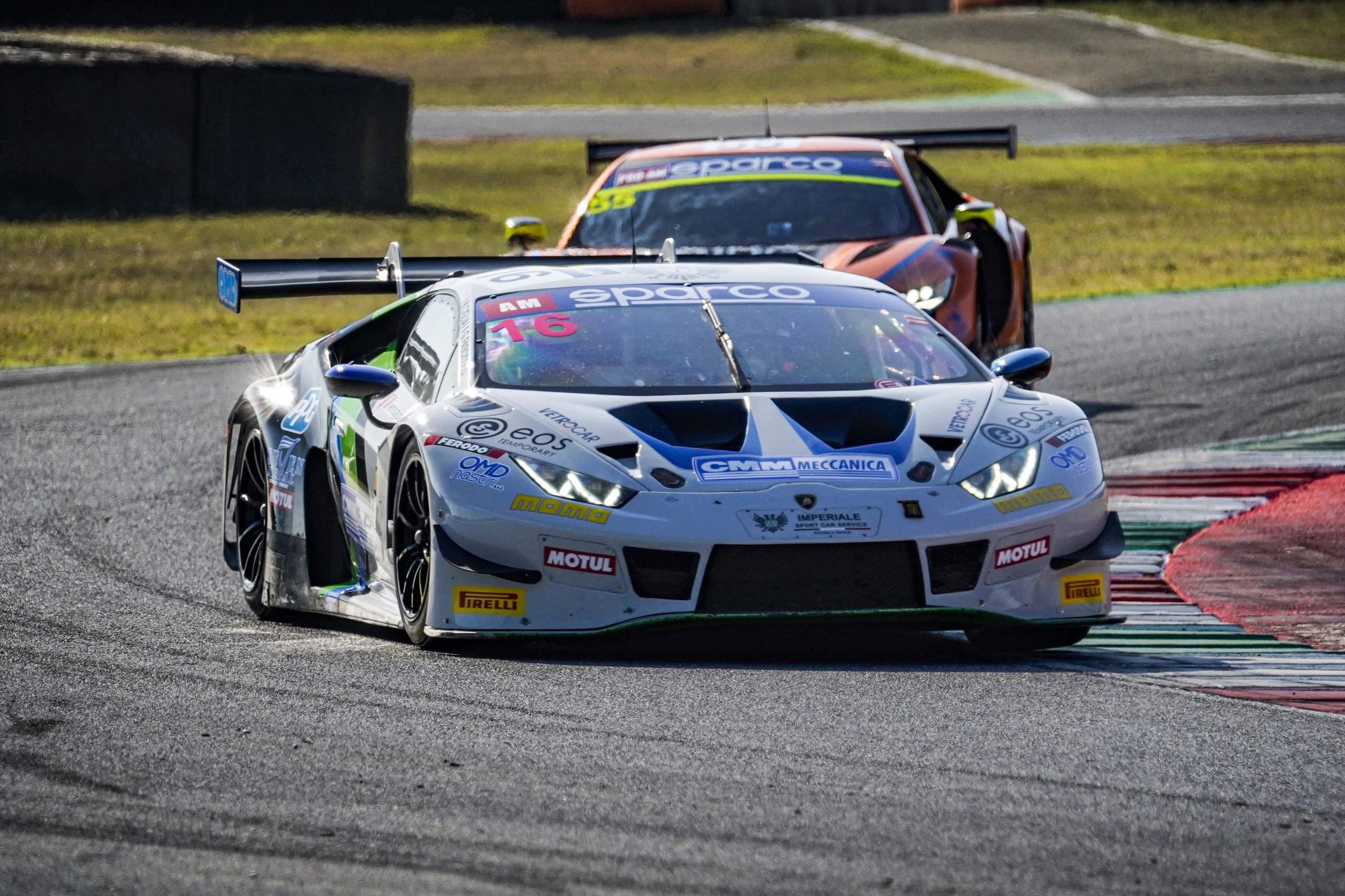 White lamborghini huracán gt3 evo2 race car navigating a turn on a racetrack with sponsor decals and large rear wing visible