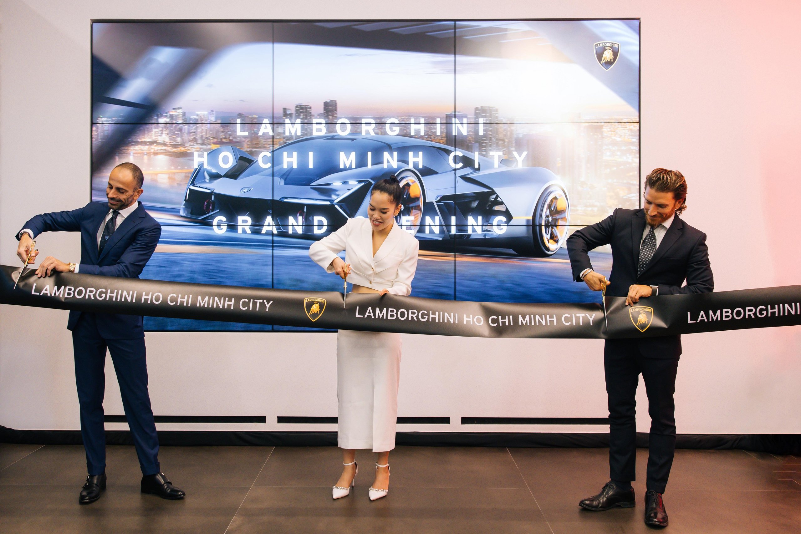 Lamborghini Plants Its Flag In Vietnam With A Ho Chi Minh City Showroom That Doubles As A 60Th Anniversary Statement 3 Three individuals cut a ceremonial ribbon during the grand opening of the lamborghini ho chi minh city dealership with a digital display in the background