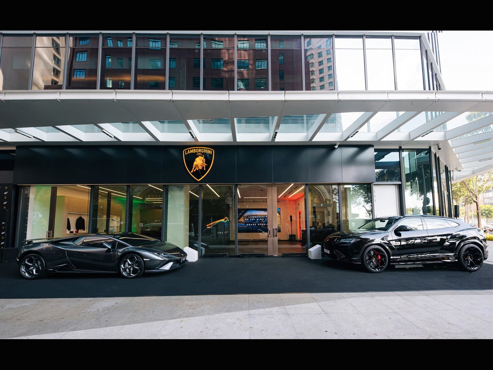 A black Lamborghini Revuelto and a black Lamborghini Urus parked outside the new Lamborghini Ho Chi Minh City showroom at the Hilton Saigon Hotel