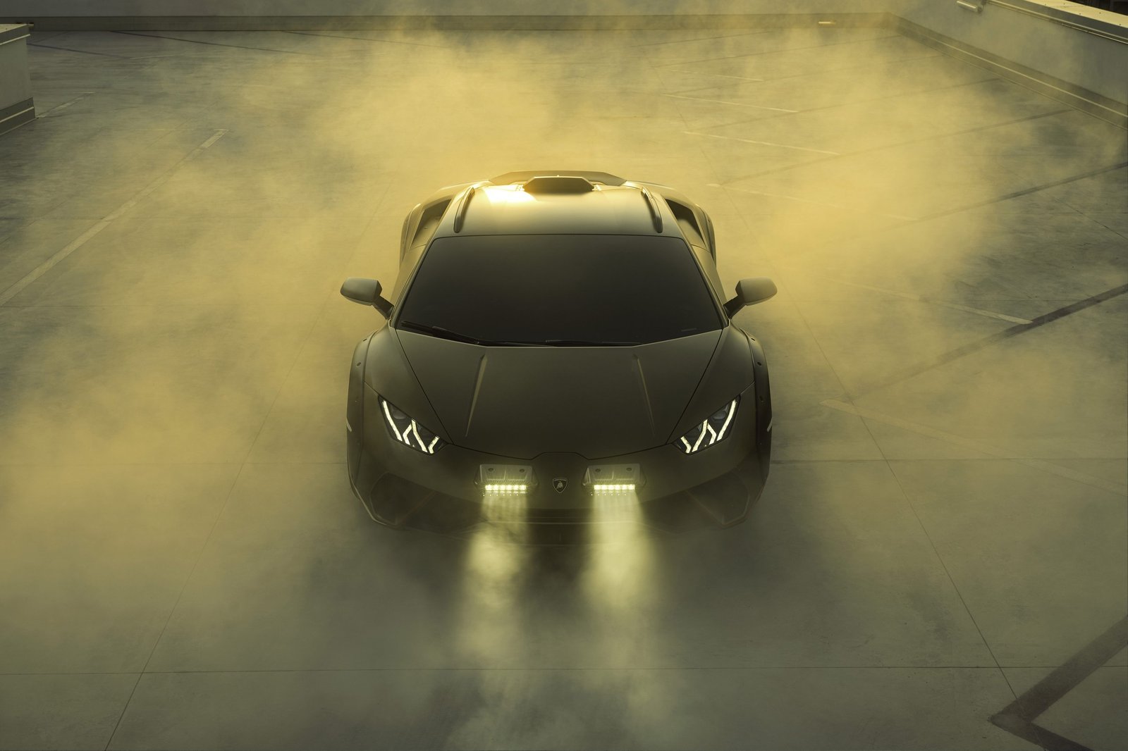 Front view of the Lamborghini Huracán Sterrato with illuminated auxiliary rally lights, wide fender flares, and elevated stance against a sunset sky