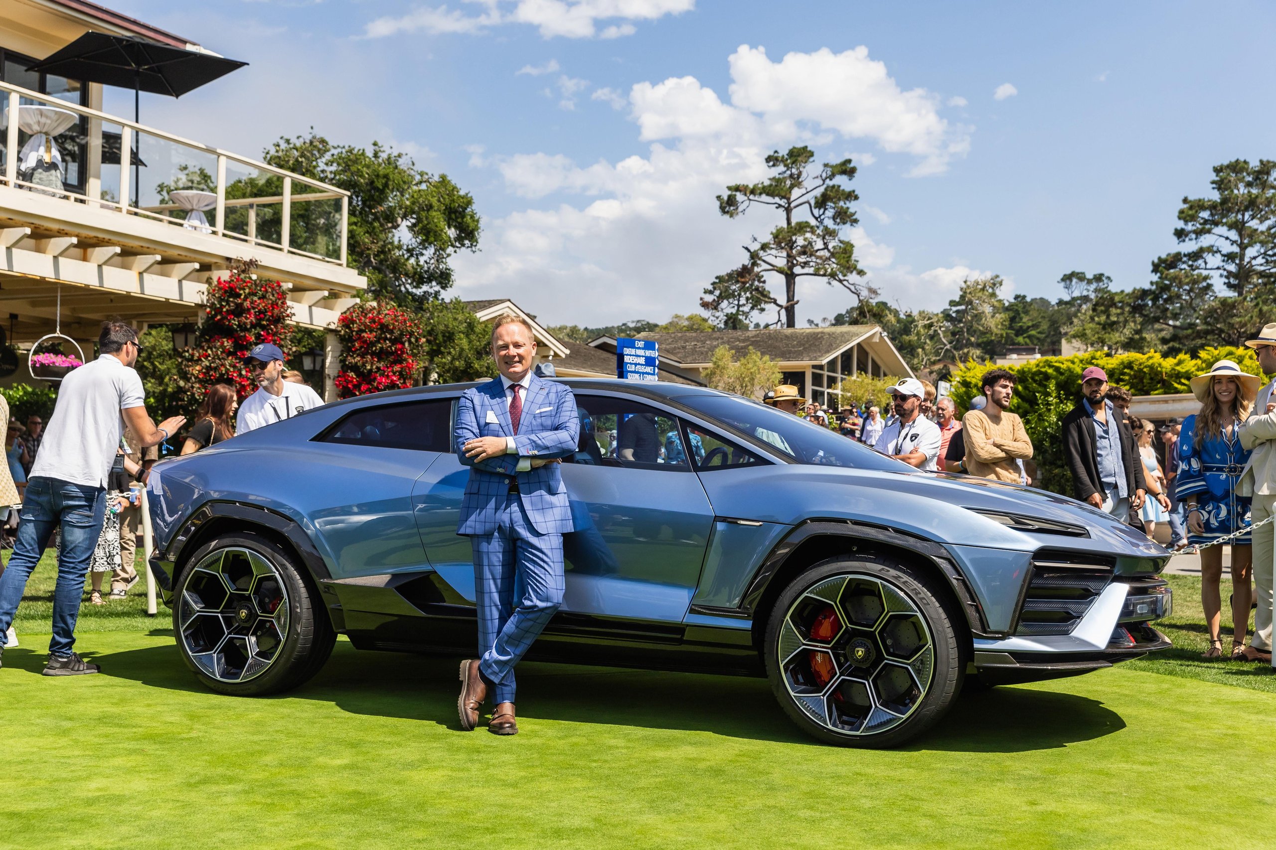 Lamborghini Killed The All-Electric Lanzador, And Its Customers Barely Flinched 7 A man in a blue plaid suit stands beside the lamborghini lanzador concept at an outdoor event, highlighting the car's futuristic suv-coupe silhouette, sharp lines, and large hexagonal wheels
