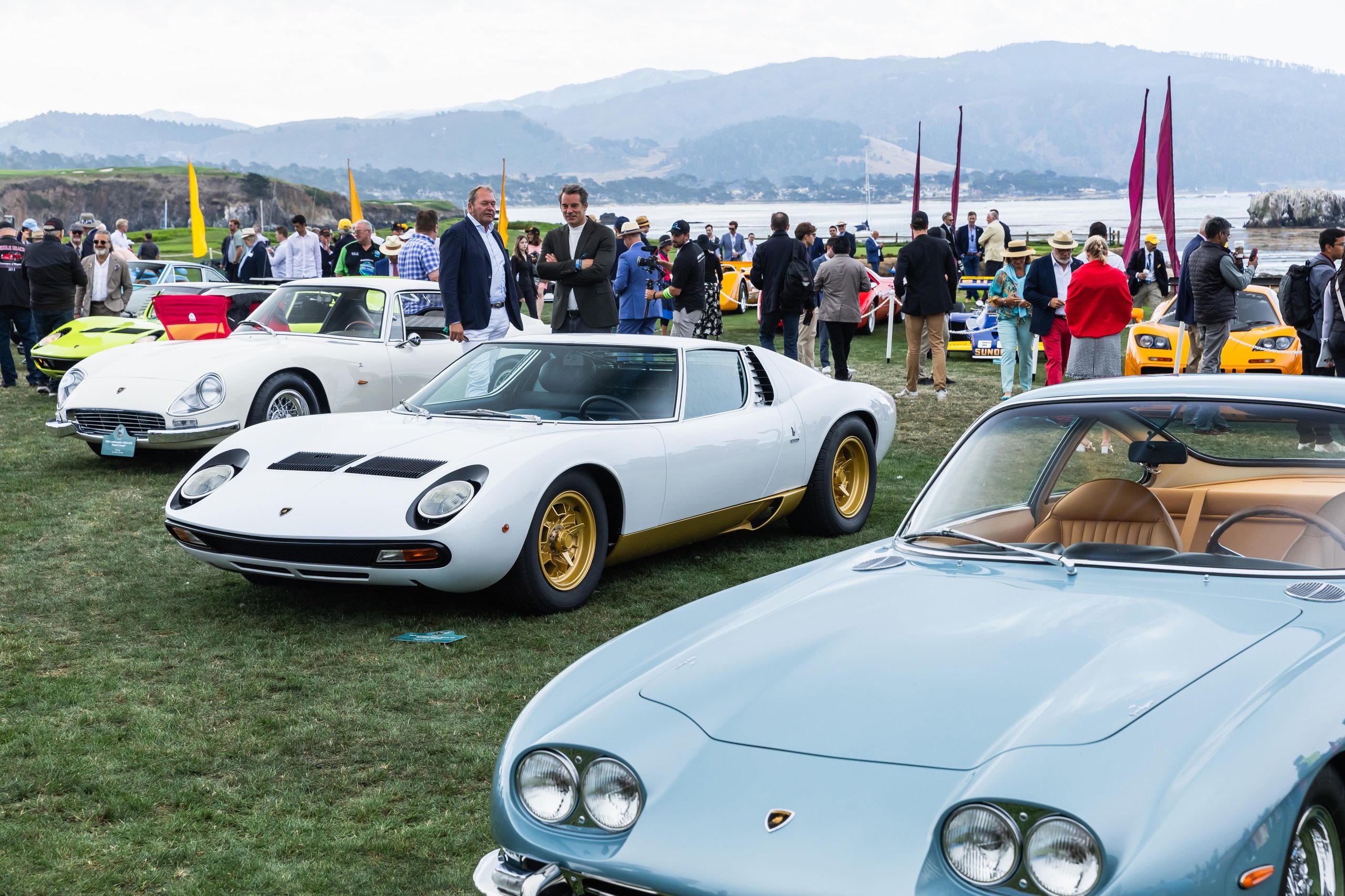 Lamborghini Killed The All-Electric Lanzador, And Its Customers Barely Flinched 9 Several classic lamborghini models including a white miura and a light blue islero displayed on the grassy field at pebble beach with spectators and mountains in the background