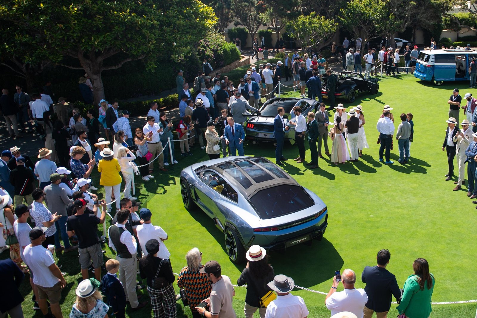 Elevated view of the Lamborghini Lanzador Concept on the Pebble Beach Concept Lawn surrounded by crowds of spectators, showing its futuristic SUV-coupe silhouette and panoramic glass roof
