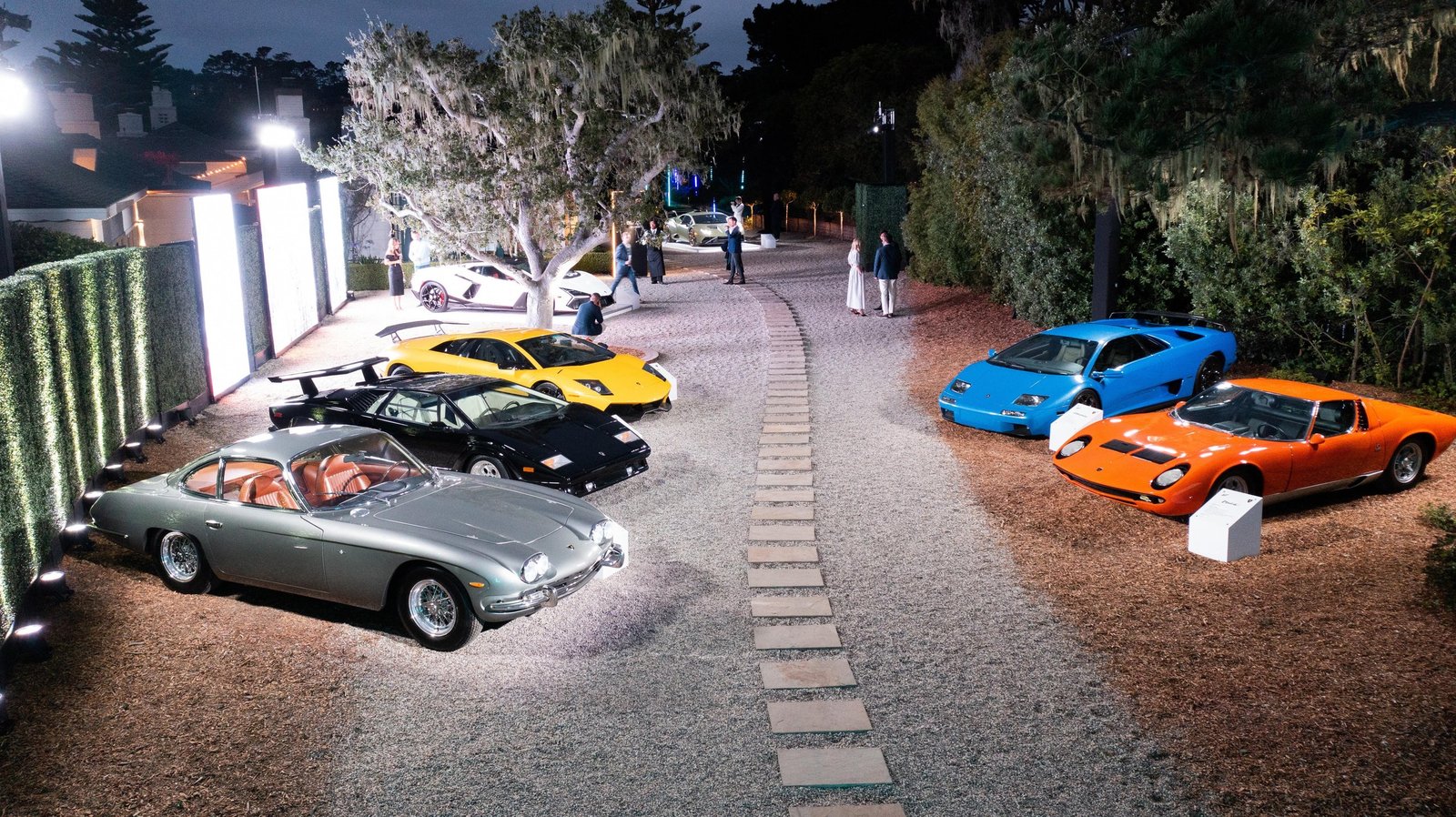 Aerial dusk view of the Lamborghini Lounge Monterey showing classic and modern Lamborghini models arranged on illuminated gravel paths at a private estate