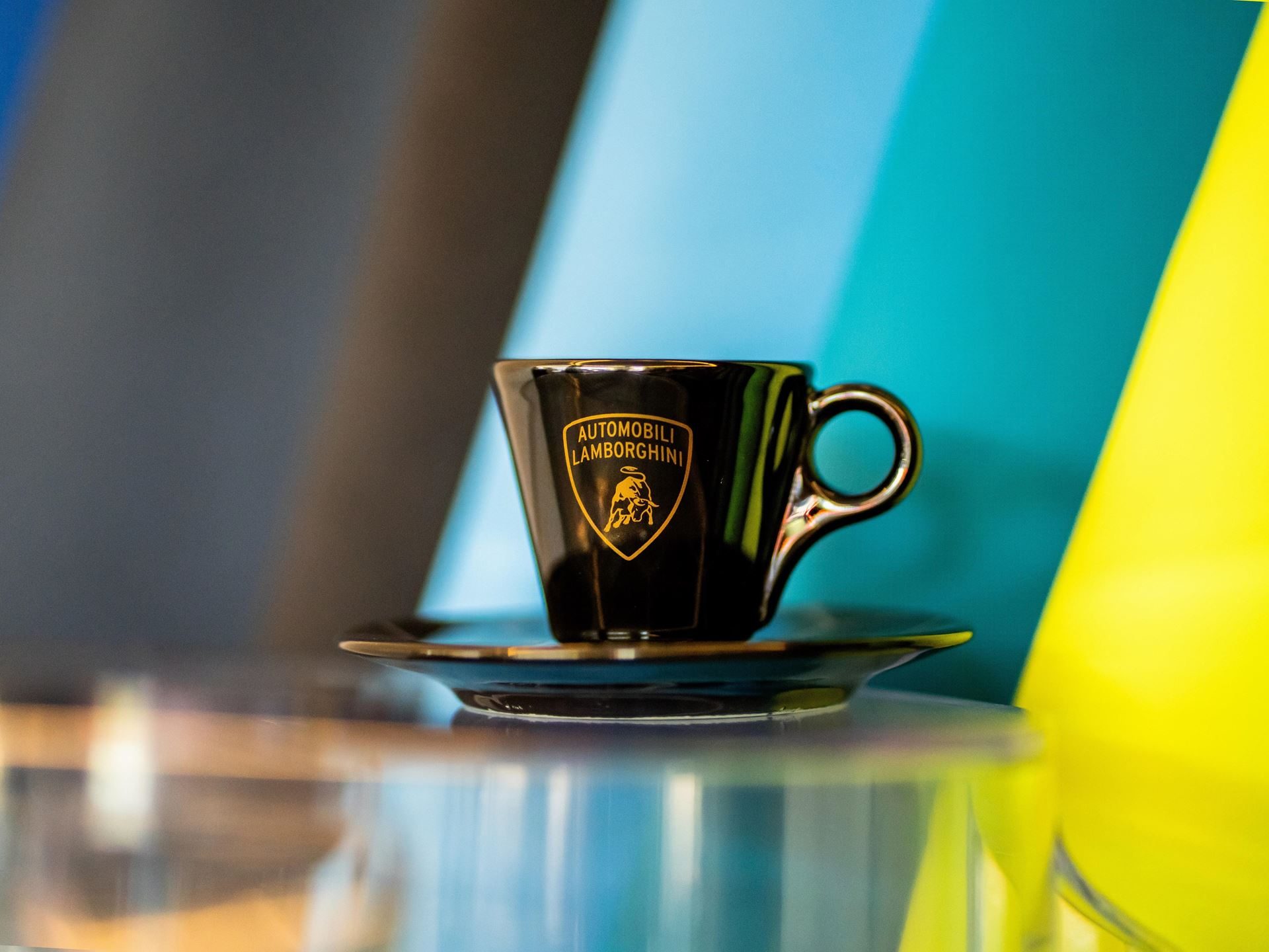 Lamborghini Partners With Lavazza To Pour Italian Luxury Beyond The Showroom 9 Black espresso cup with gold automobili lamborghini logo and shield on a saucer against a colorful geometric background