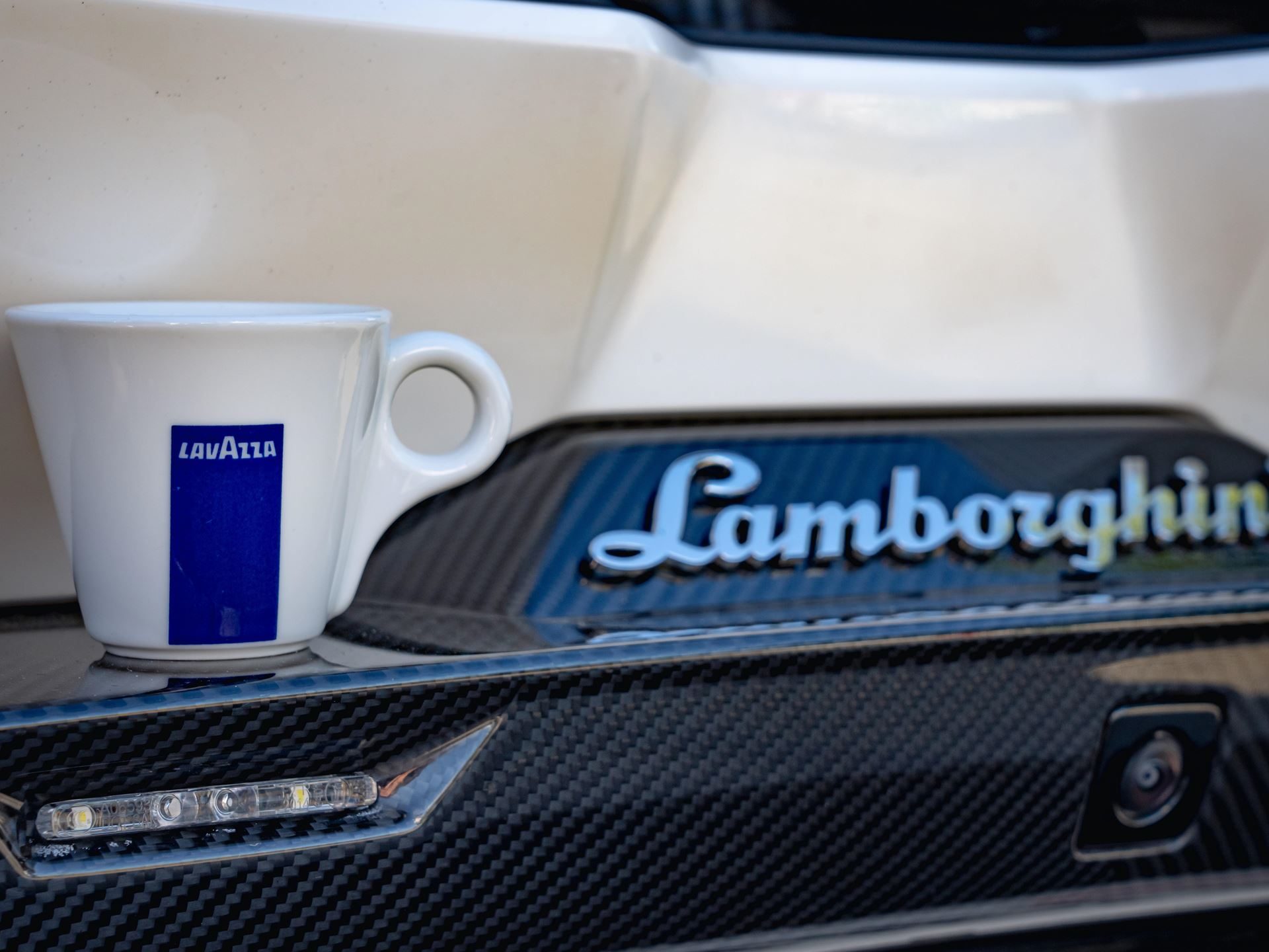 Lamborghini Partners With Lavazza To Pour Italian Luxury Beyond The Showroom 11 White lavazza espresso cup on the carbon fiber rear deck of a white lamborghini with the lamborghini script badge visible