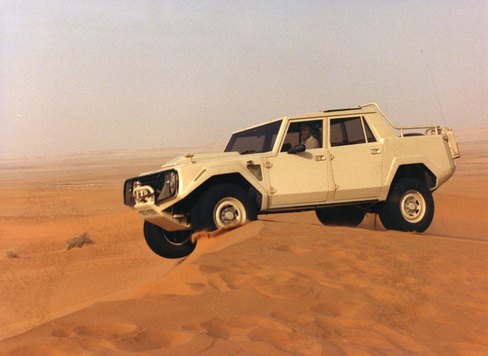 White Lamborghini LM002 mid-air over a sand dune in the desert