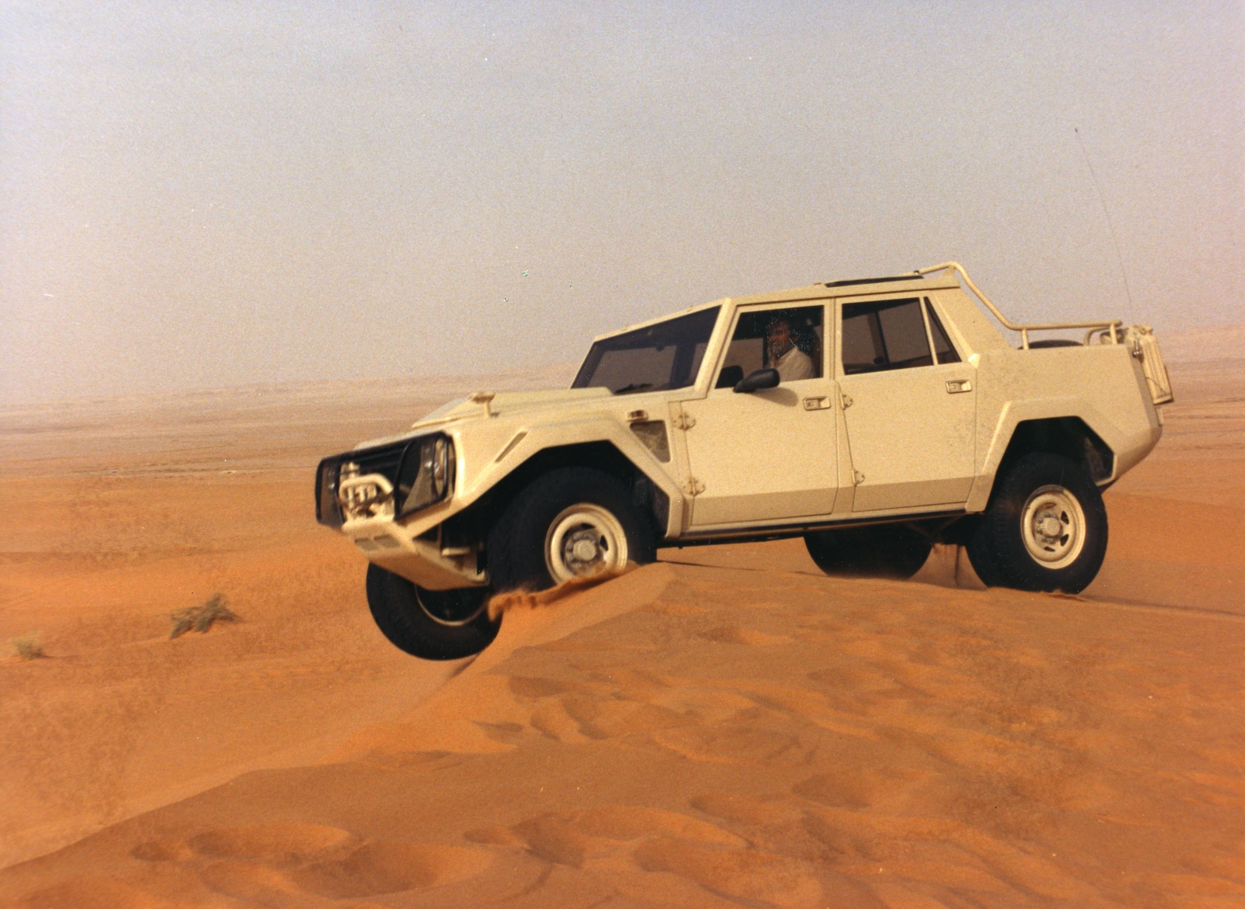 White lamborghini lm002 mid-air over a sand dune in the desert