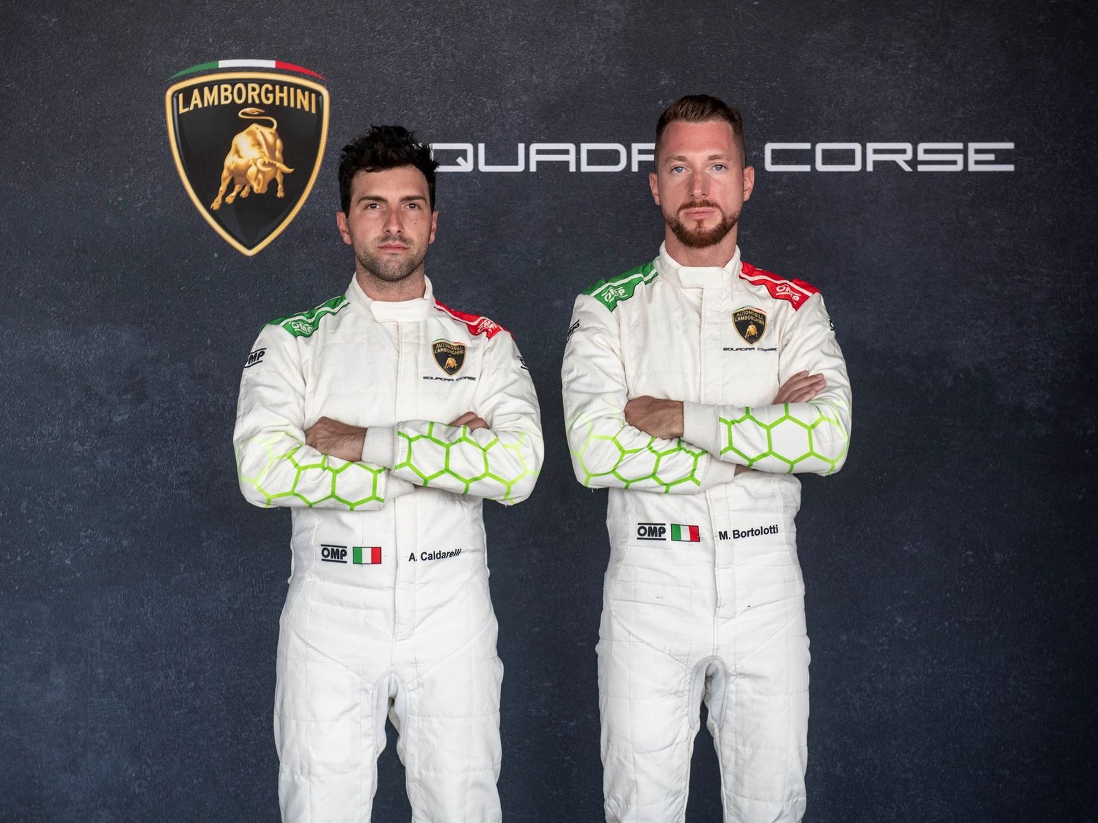 Andrea Caldarelli and Mirko Bortolotti in Lamborghini Squadra Corse racing suits, arms crossed, standing side by side against a dark backdrop with the Lamborghini and Squadra Corse logos