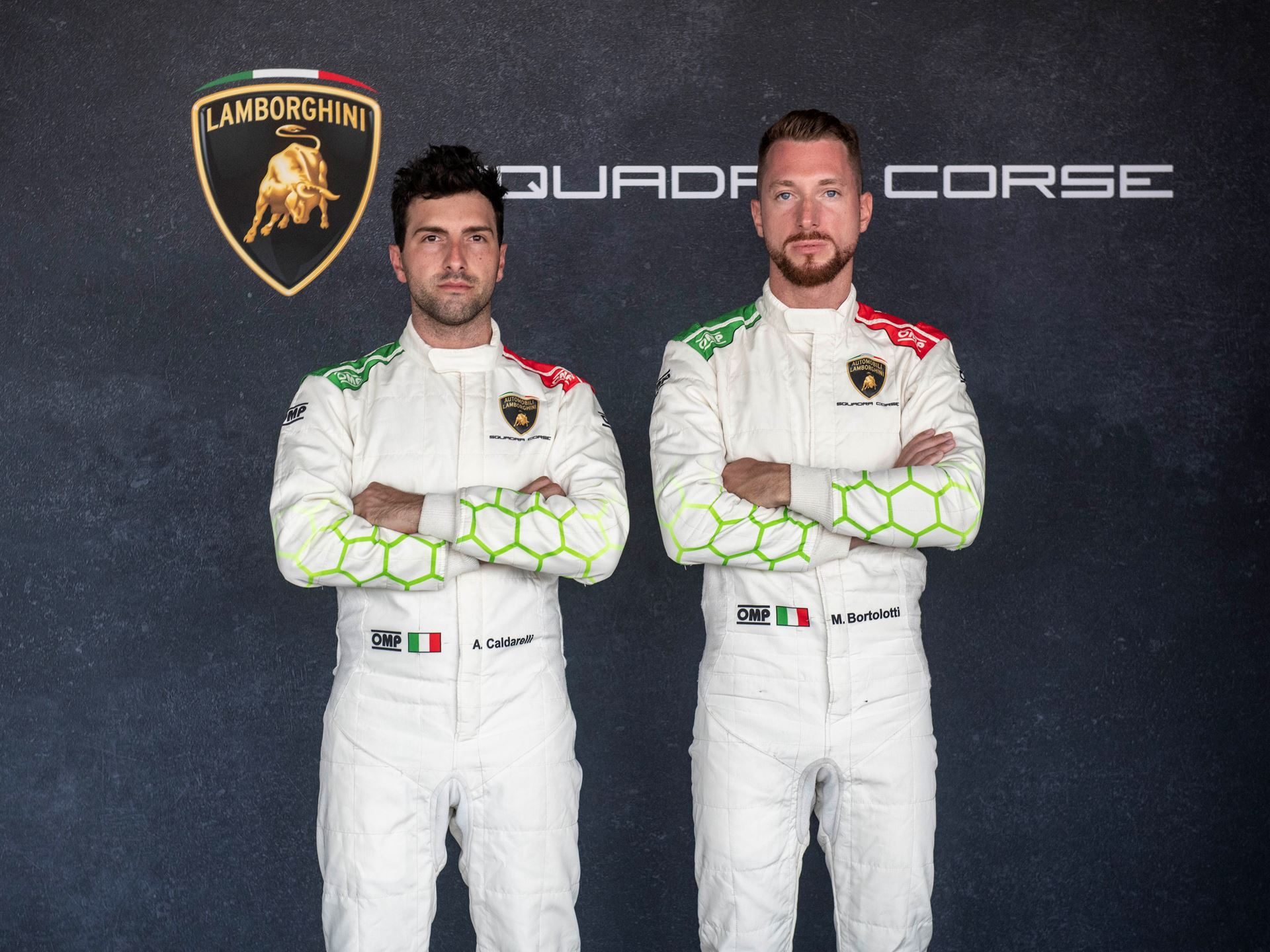 Andrea caldarelli and mirko bortolotti in lamborghini squadra corse racing suits, arms crossed, standing side by side against a dark backdrop with the lamborghini and squadra corse logos
