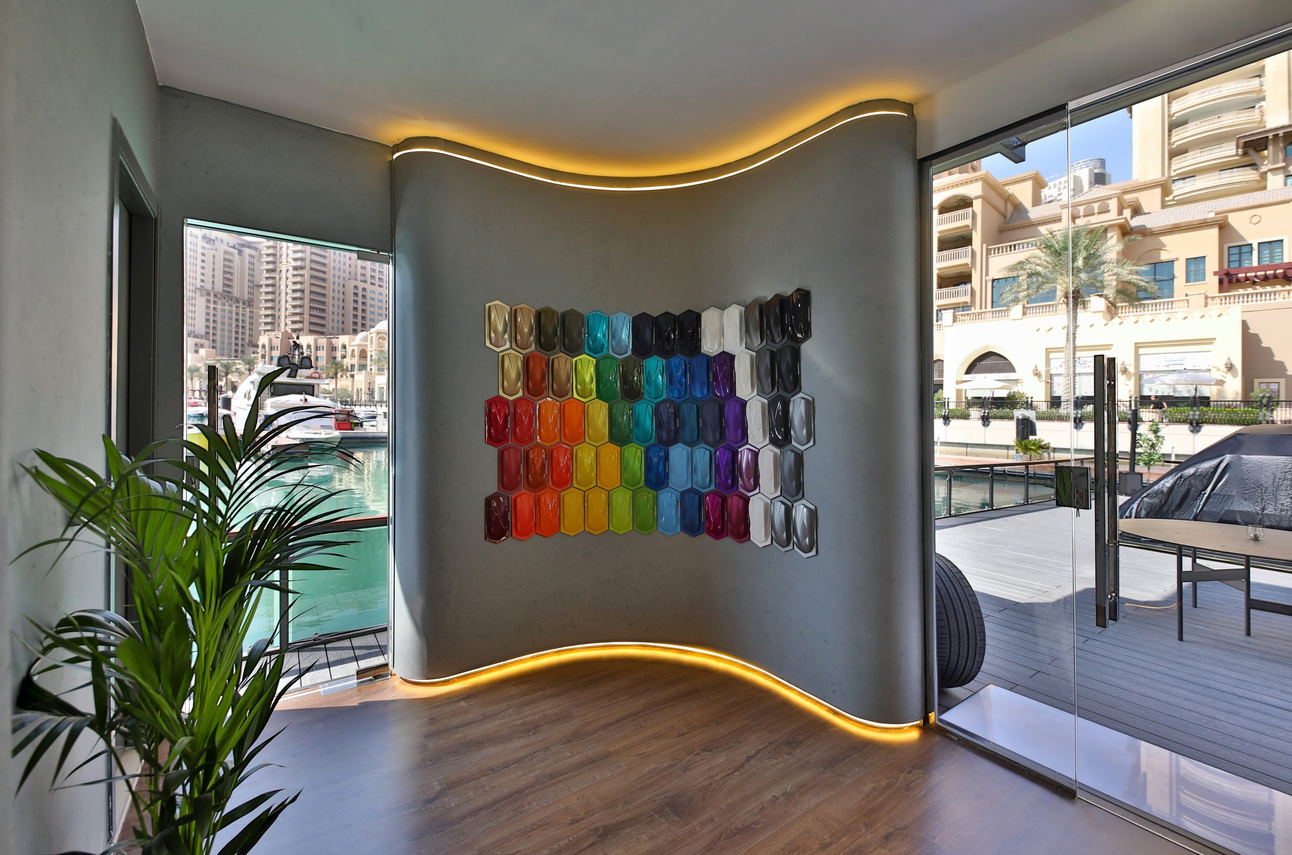 Vibrant wall display of hexagonal color samples showcasing lamborghini's ad personam customization palette with waterfront views visible through the window