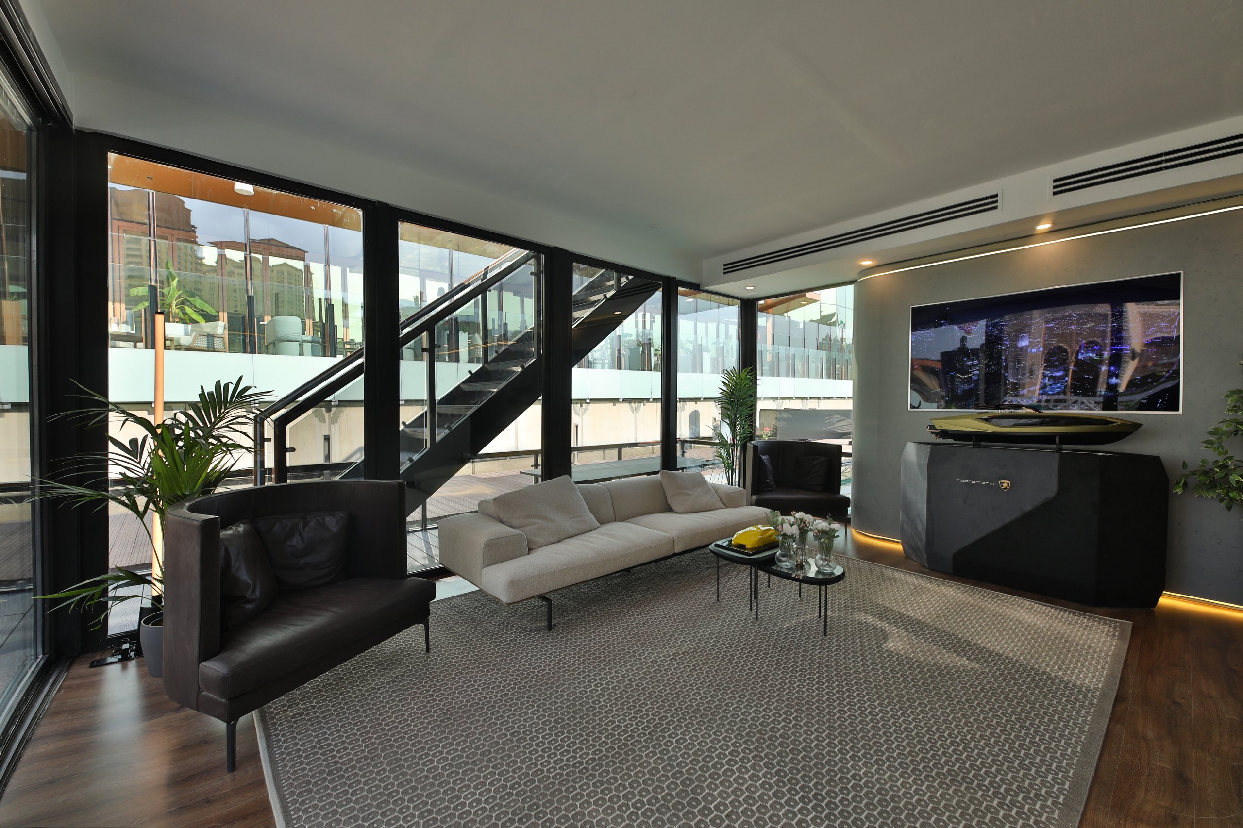 Interior of the lamborghini lounge doha showing modern sofas, a large display screen, and a scale model on a stand in a minimalist luxury setting