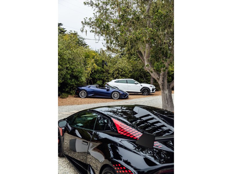 A black Lamborghini Sián FKP 37, blue Huracán Evo Spyder, and white Urus displayed outdoors at the Lamborghini Lounge Monterey