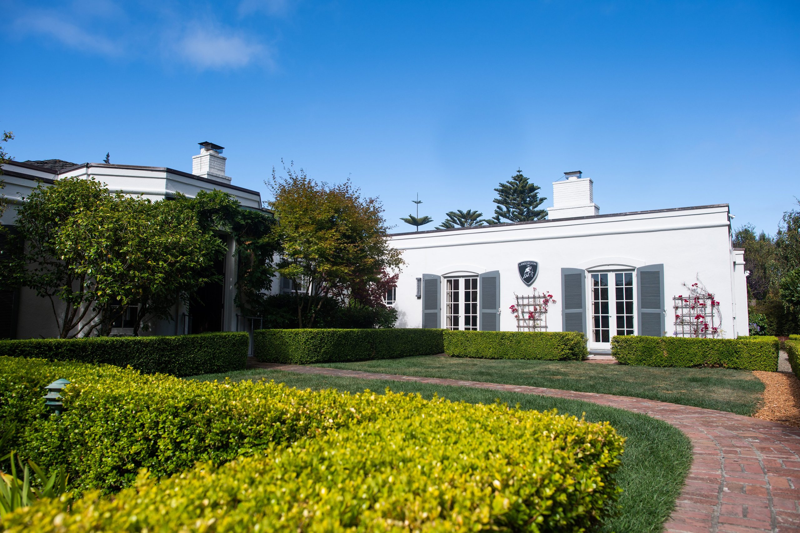 Inside Lamborghini'S Lounge Monterey: Where The Urus Performante Debut Became A Masterclass In Selling A Lifestyle 13 Exterior of the white lamborghini lounge monterey building with lamborghini shield logo above the window, green hedges, and blue sky