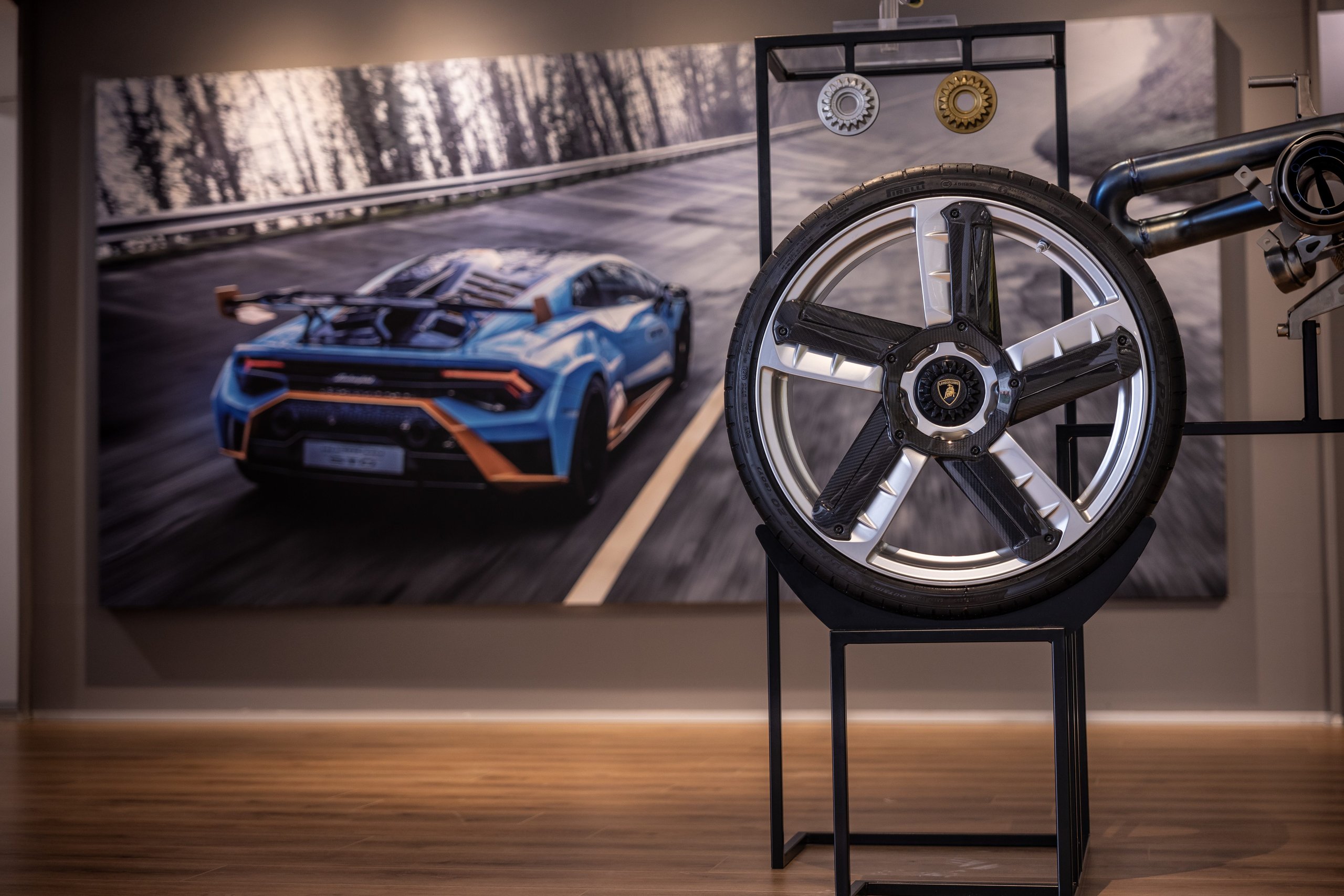 Porto Cervo'S Lamborghini Lounge: Where Ad Personam Meets The Sardinian Coast 9 Lamborghini huracán sto wheel assembly on display with a backdrop image of a blue sto on a winding road
