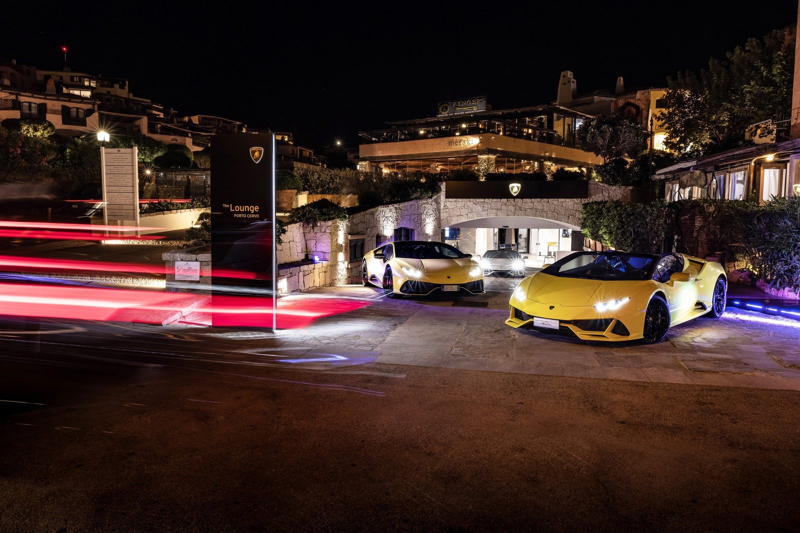 Yellow Lamborghini Huracán Evo Spyder and white Huracán STO parked outside the Lamborghini Lounge in Porto Cervo at night