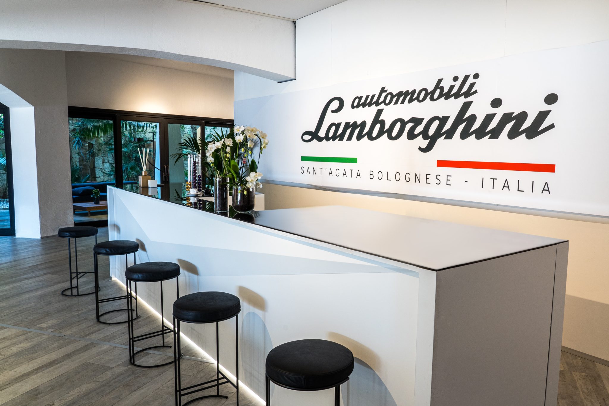 Lamborghini'S Porto Cervo Pop-Up Is A Masterclass In Selling The Supercar Life, Not Just Supercars 3 Angular white reception desk with automobili lamborghini branding at the porto cervo lounge