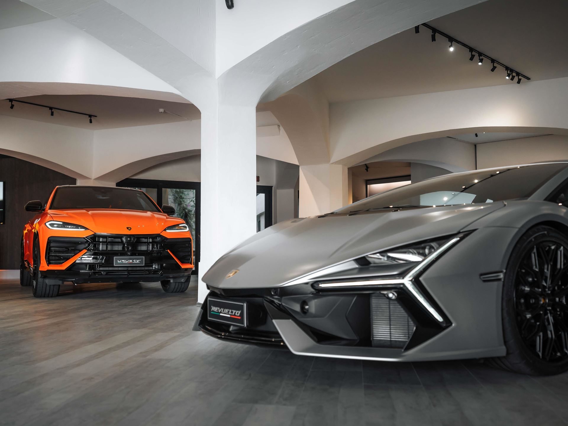 Lamborghini'S Porto Cervo Lounge Returns For A Sixth Summer As A Seaside Brand Hub 5 Orange lamborghini urus se parked behind grey lamborghini revuelto in the porto cervo lounge showroom with white arched ceilings