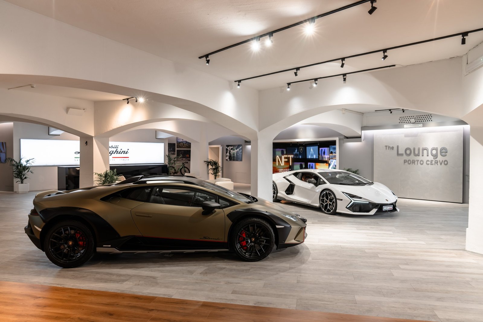 Gold Huracán Sterrato and white Revuelto displayed side by side inside The Lounge Porto Cervo with arched doorways