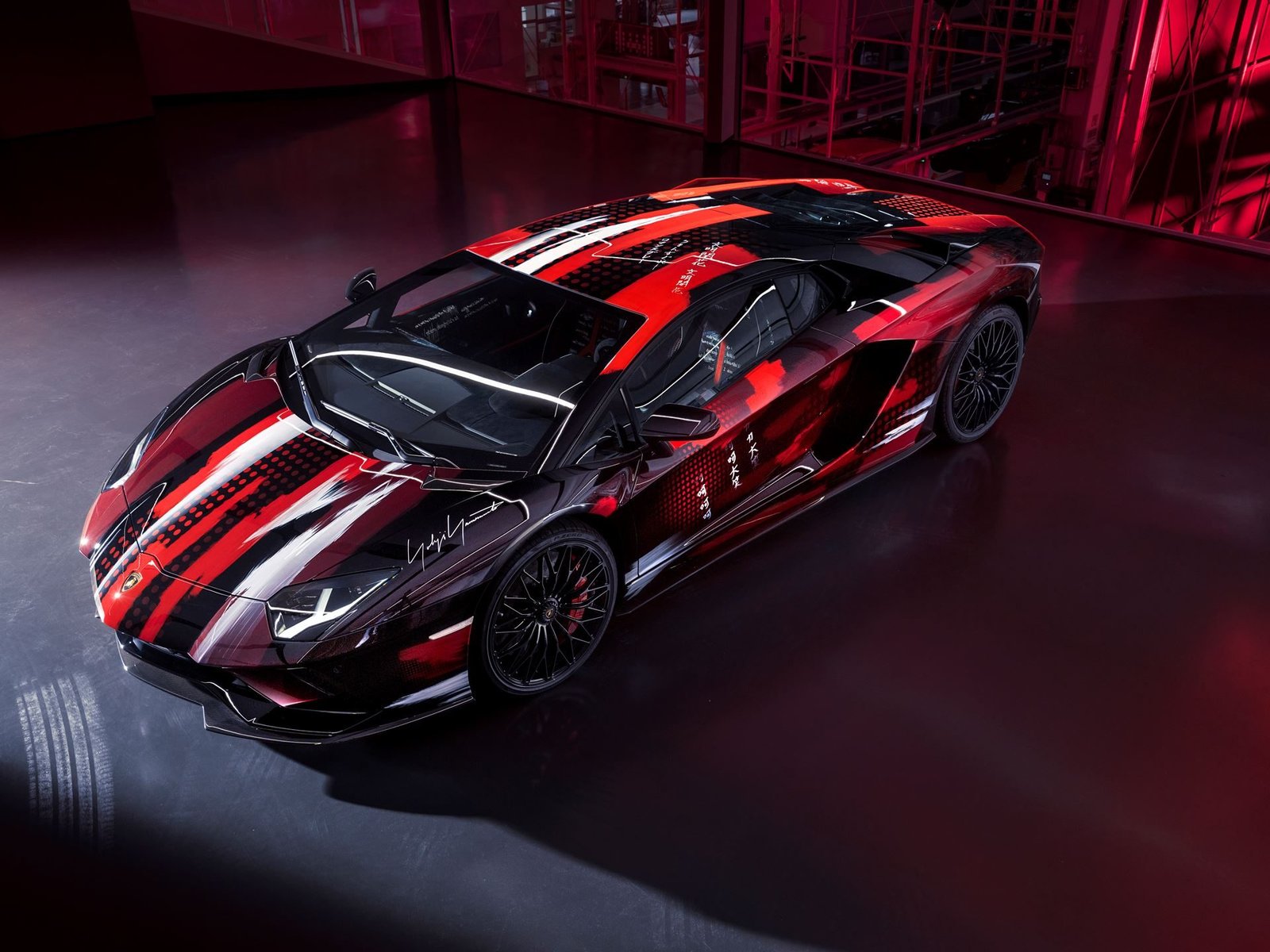 Overhead view of the Yohji Yamamoto Aventador S showing the black, red, and white abstract livery and Japanese lettering on the bodywork