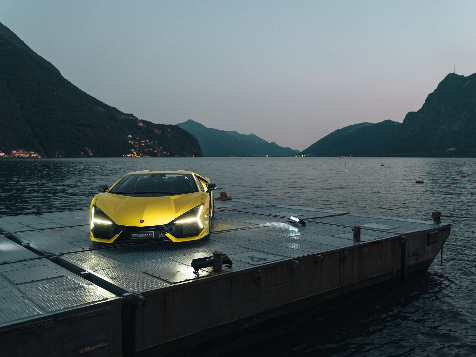 Lamborghini Lugano Turned Its First Birthday Into A Lakeside Stage For The Urus Se'S Swiss Debut 9 Yellow lamborghini revuelto on a floating platform on lake lugano at dusk with headlights illuminated and mountains in the background