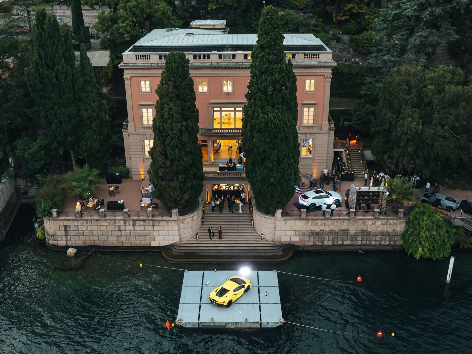 Aerial view of Villa Heleneum on Lake Lugano with a yellow Lamborghini Revuelto on a floating platform and a white Urus SE on the terrace during the anniversary event