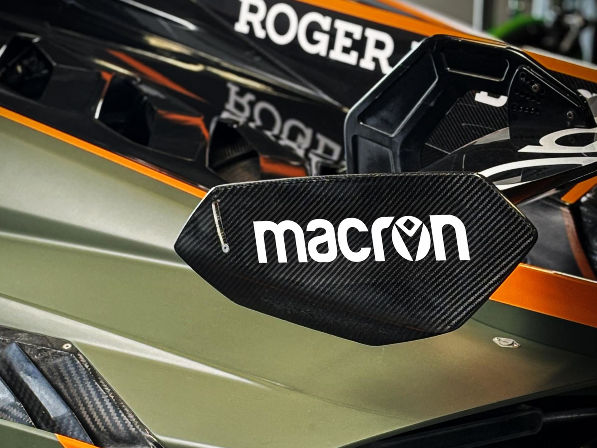 Lamborghini Taps Macron To Outfit Squadra Corse For Three Seasons, Replica Collection Included 11 Close-up of a carbon fiber aerodynamic element on a green and orange lamborghini huracán gt3 evo2 showing the macron logo