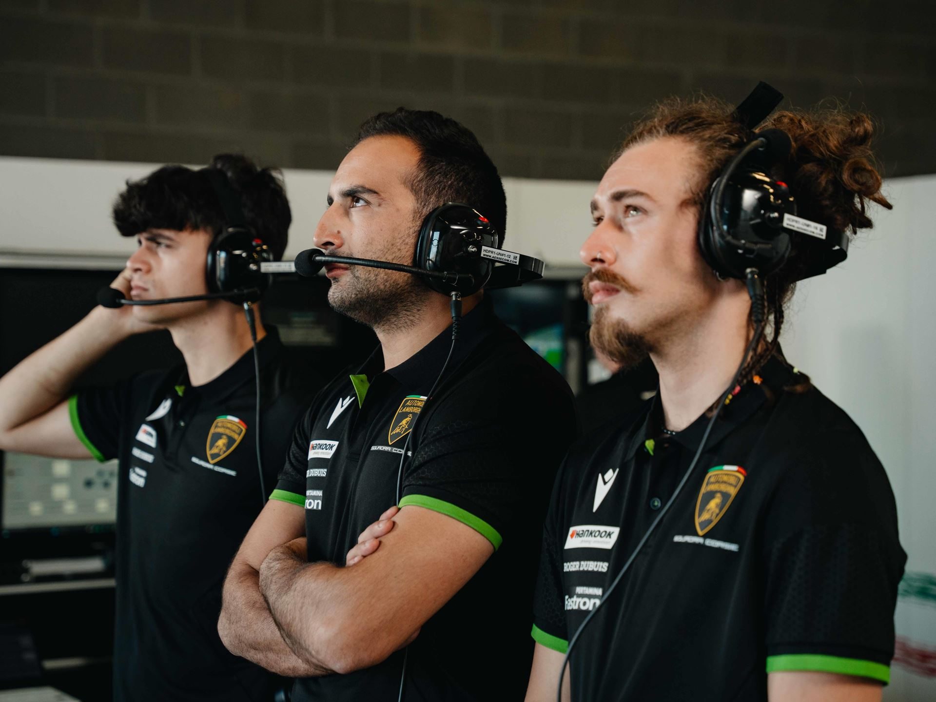 Lamborghini Taps Macron To Outfit Squadra Corse For Three Seasons, Replica Collection Included 5 Three lamborghini squadra corse pit crew members in black macron team shirts and headsets watch a race intently from the pit garage