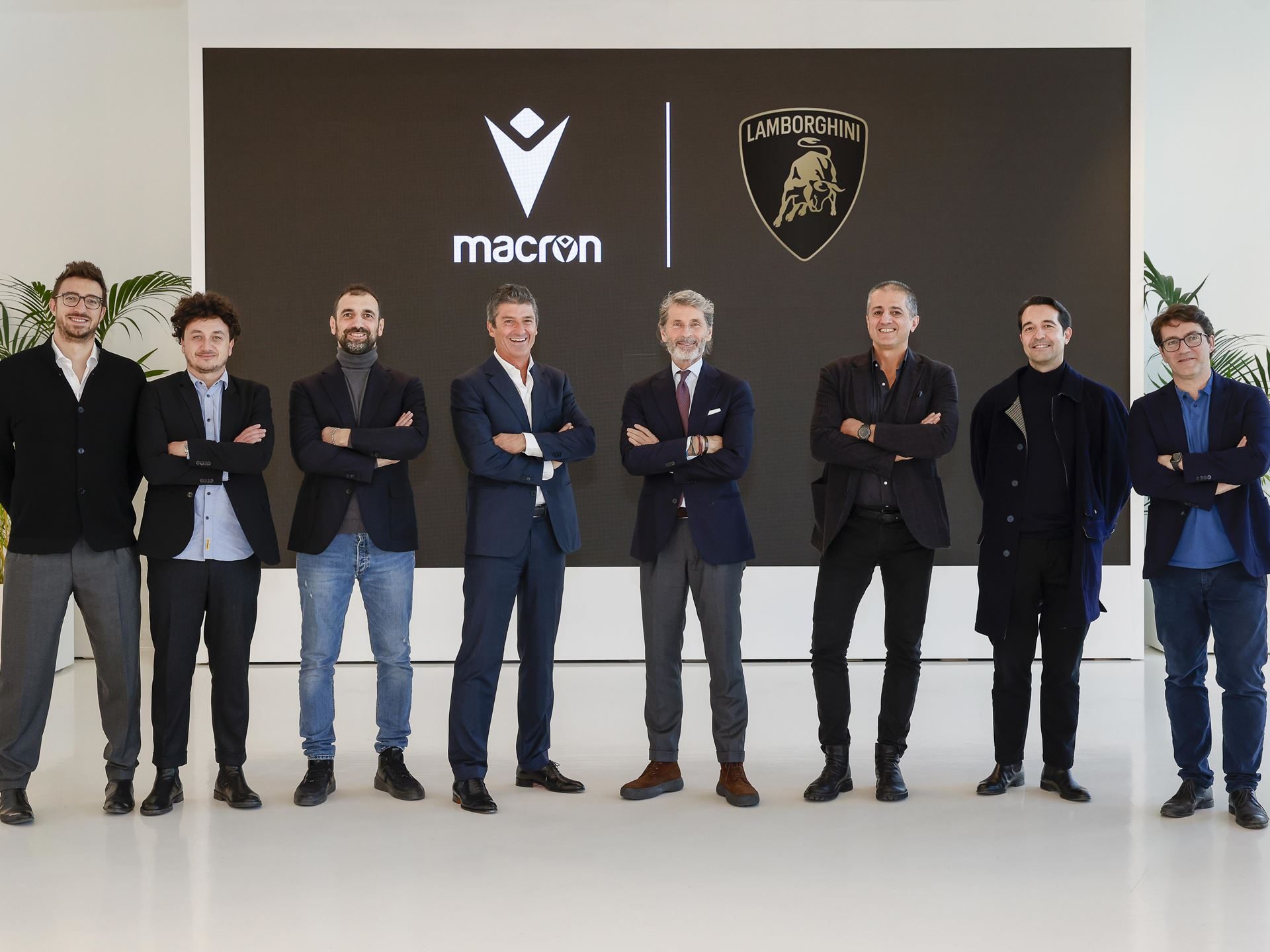 Lamborghini Taps Macron To Outfit Squadra Corse For Three Seasons, Replica Collection Included 7 A group of seven executives and team members stand with arms crossed in front of a screen displaying macron and lamborghini logos