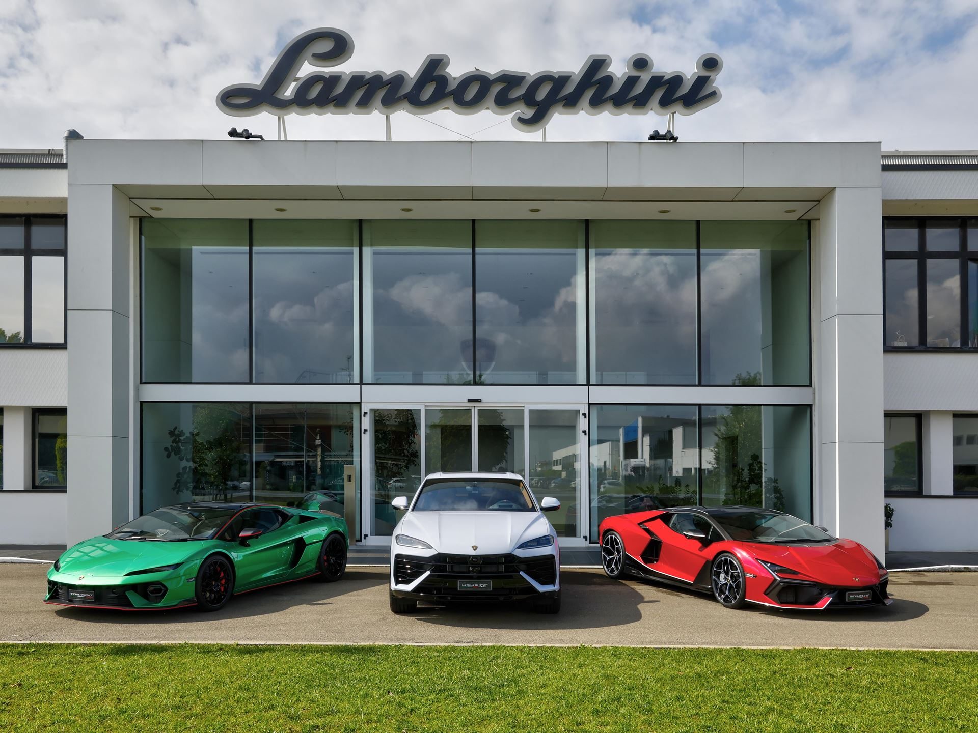 Why Lamborghini'S 'Made In Italy' Day Matters More Than National Pride 5 White lamborghini urus, green huracán, and red revuelto parked in front of the lamborghini headquarters building with logo