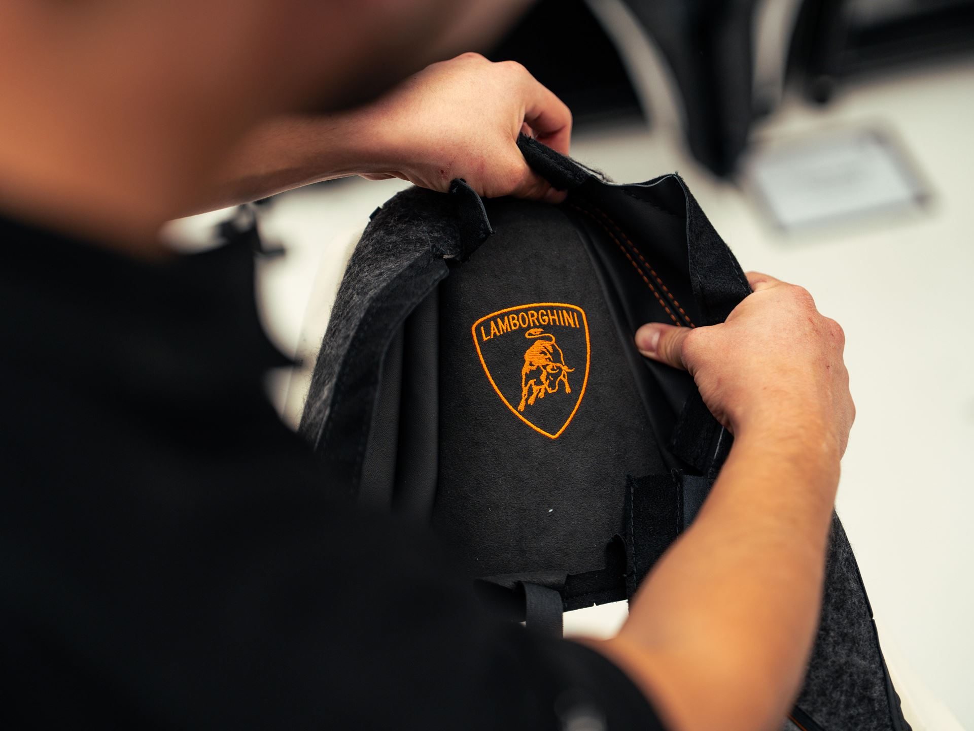 Why Lamborghini'S 'Made In Italy' Day Matters More Than National Pride 3 Close-up of hands embroidering an orange lamborghini logo onto black material during the manufacturing process