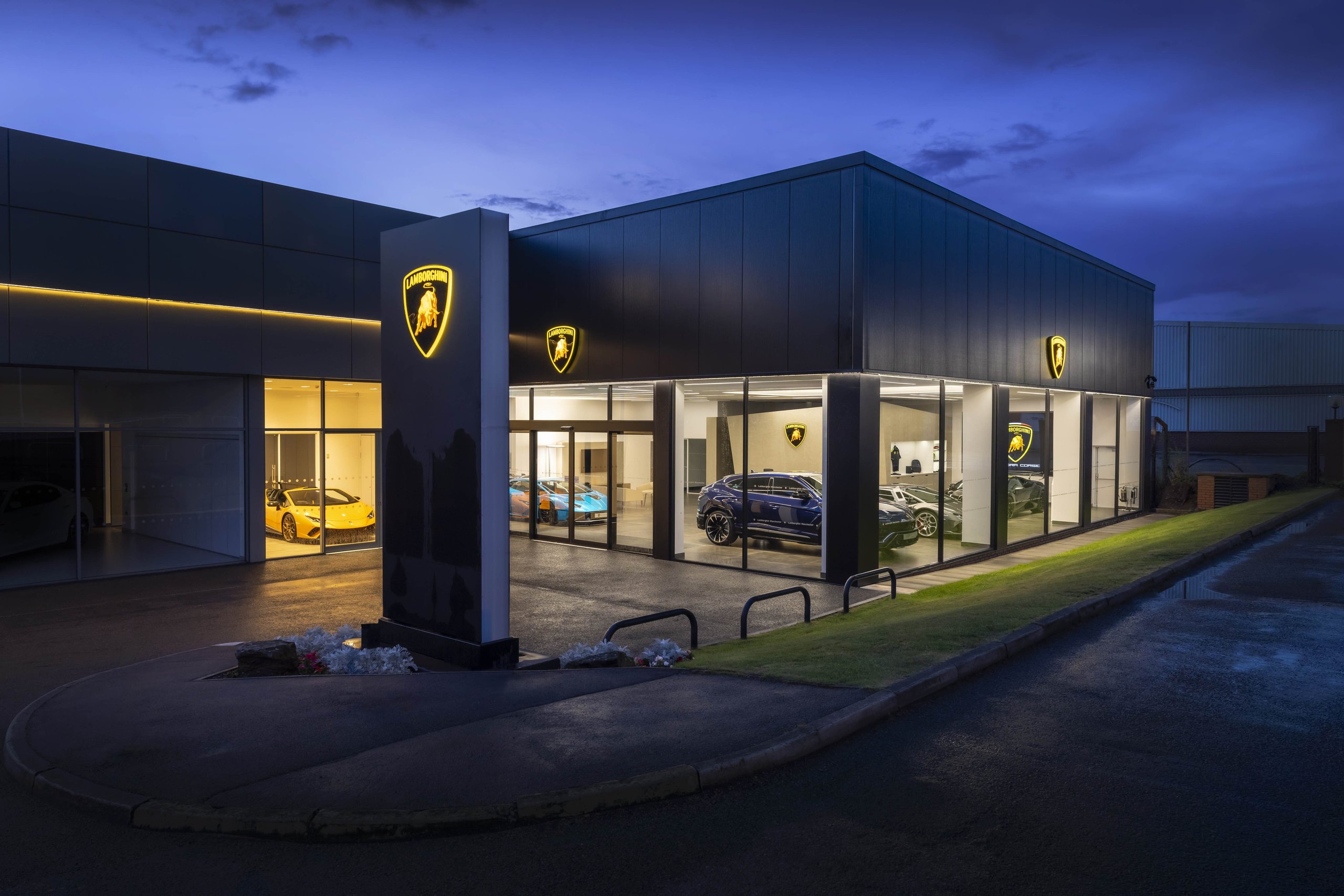 Lamborghini Manchester'S New Stockport Showroom Signals Where The Brand Is Placing Its Uk Bets 11 Evening exterior view of the illuminated lamborghini manchester showroom with multiple lamborghini models visible through large glass windows