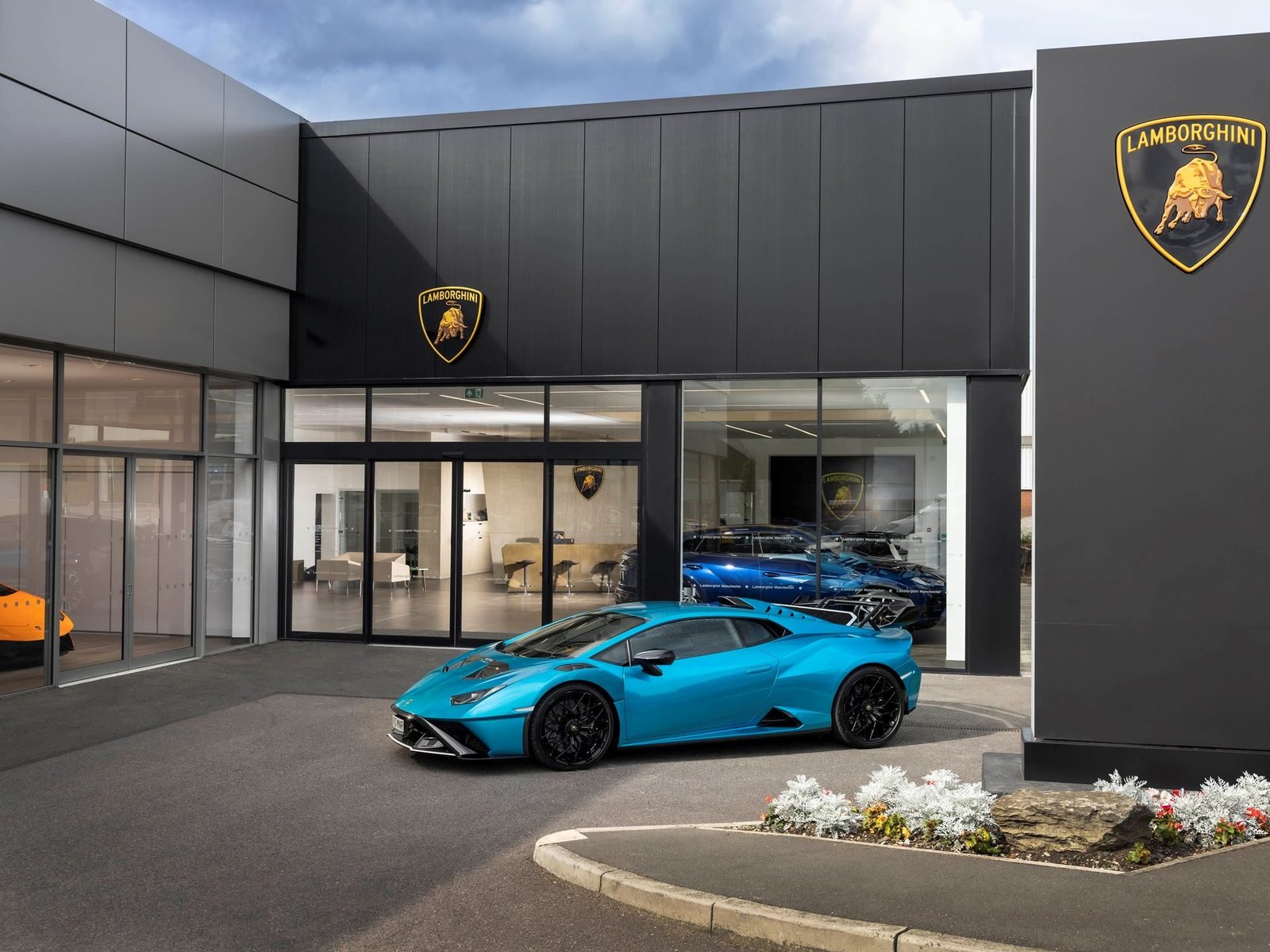 Blue Lamborghini Huracán STO parked outside the new Lamborghini Manchester showroom in Stockport, with vehicles visible through large glass windows