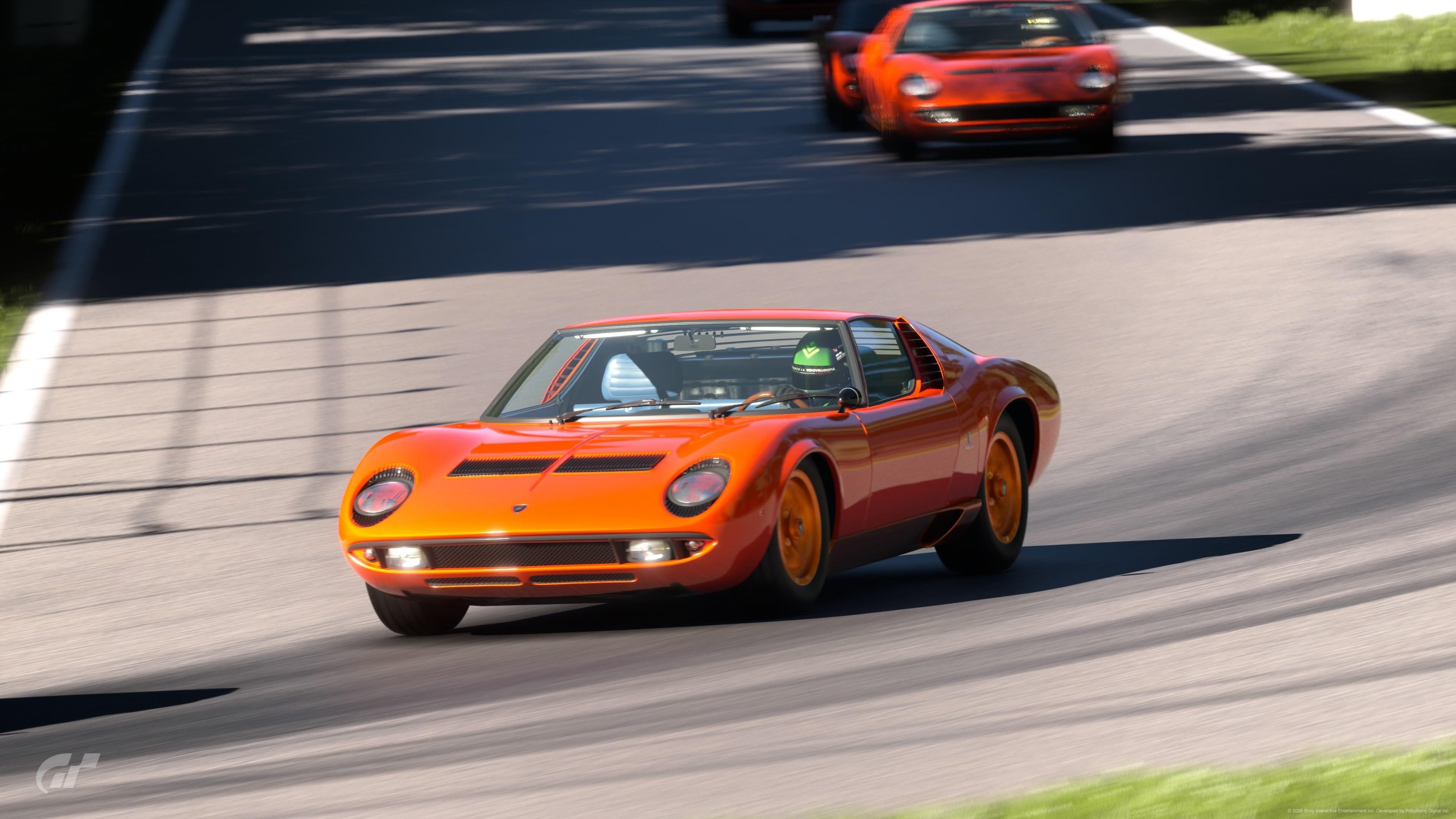 An orange lamborghini miura driven by a helmeted driver speeds around a bend on a virtual race track with another miura in the background