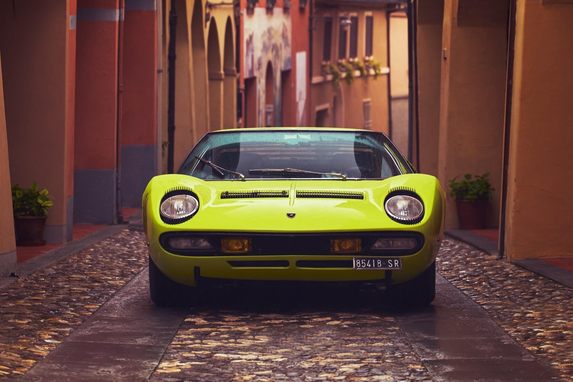 A lime green lamborghini miura p400 parked on a wet cobblestone street in a narrow european alleyway
